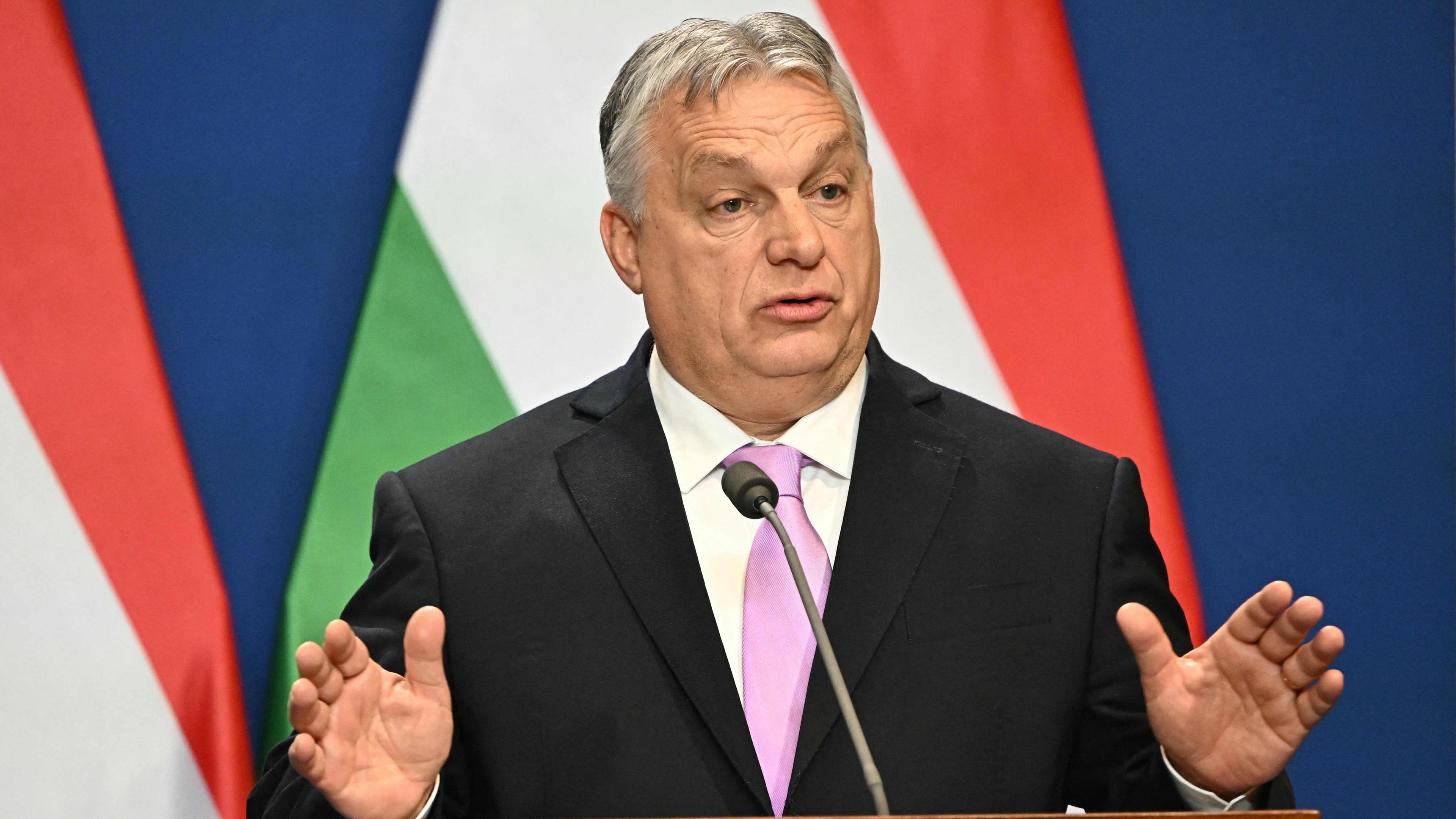 Viktor Orbán steht vor der ungarischen Flagge an einem Rednerpult und spricht.