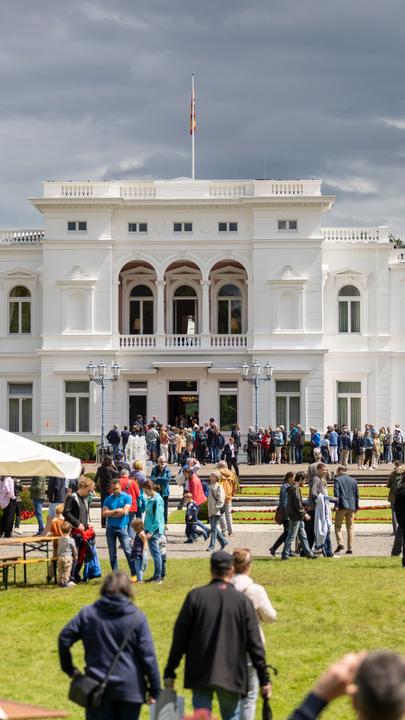Villa Hammerschmidt in Bonn. Menschen laufen auf der Rasenfläche vor der Villa her