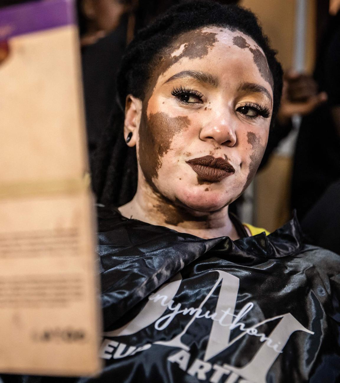 Das Vitiligo-Model Julie Nasuju betrachtet sich in einem tragbaren Spiegel, nachdem sie sich geschminkt hat.