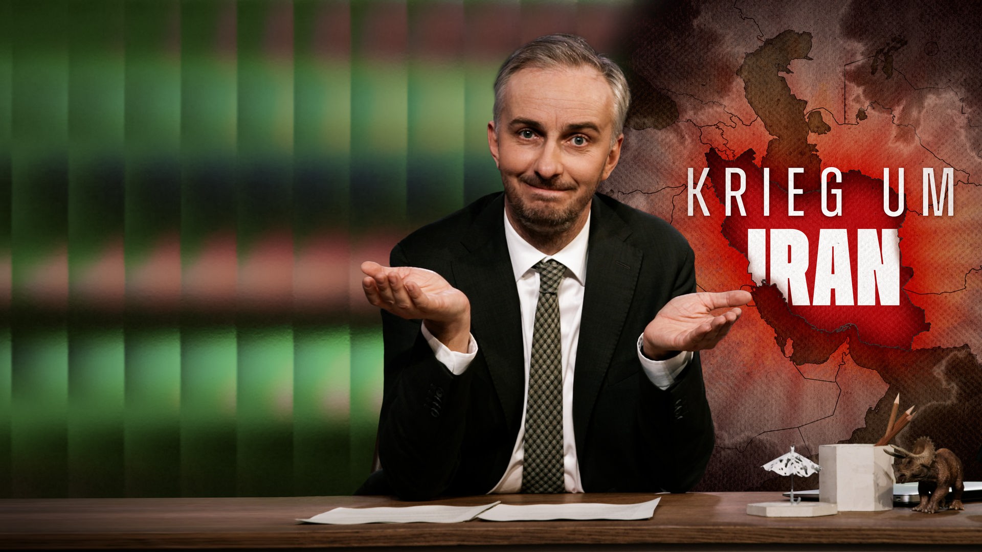 Jan Böhmermann sitzt am Schreibtisch. Rechts im Hintergrund ist eine Landkarte mit dem geografischen Umriss Irans zu sehen. Darüber steht der Text "Krieg um Iran".