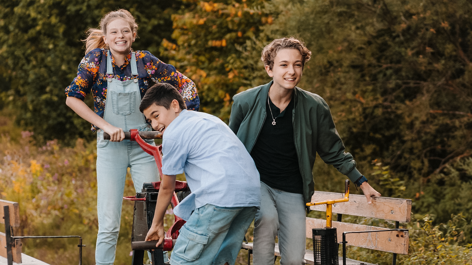 Charly (links), Hamid (Mitte) und Benny (rechts) fahren eine Draisine. Die drei Freunde lachen, sie wirken glücklich und ausgelassen.
