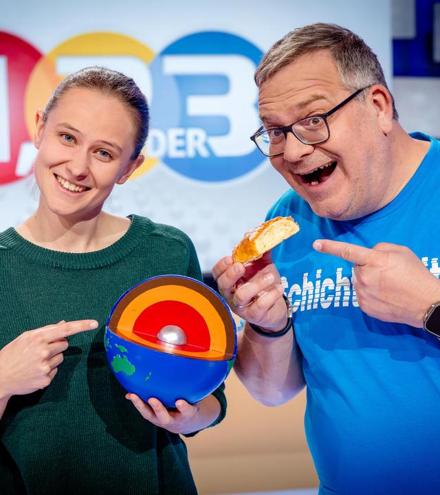 Elton steht mit Geologin Alicia Rohnacher zusammen. Sie hält ein Modell des Erdmantels vor sich. Elton und sie deuten darauf.
