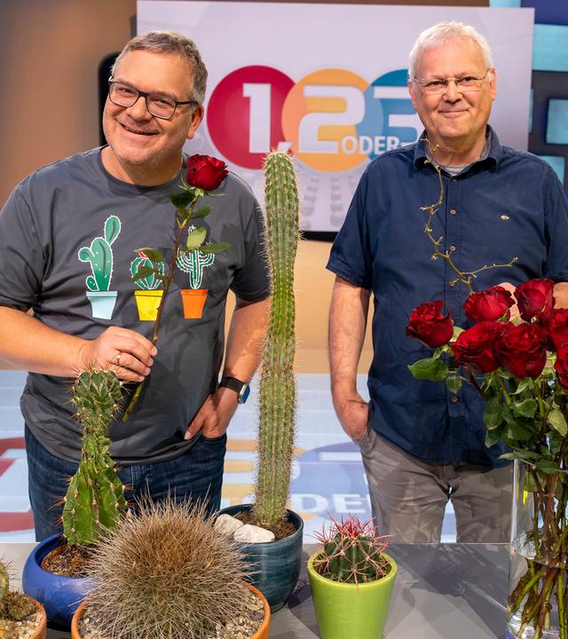Elton und Professor Christoph Neinhuis stehen hinter einem Tisch, auf dem ein Rosenstrauß in einer Vase und mehrere unterschiedlich große Kakteen platziert sind.