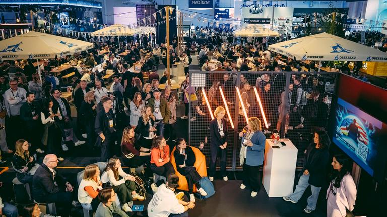 Vogelperspektive auf den gut besuchten ZDF-Stand auf der OMR-Messe 2025 in Hamburg. Im Umfeld viele Messebesucher in der Halle.