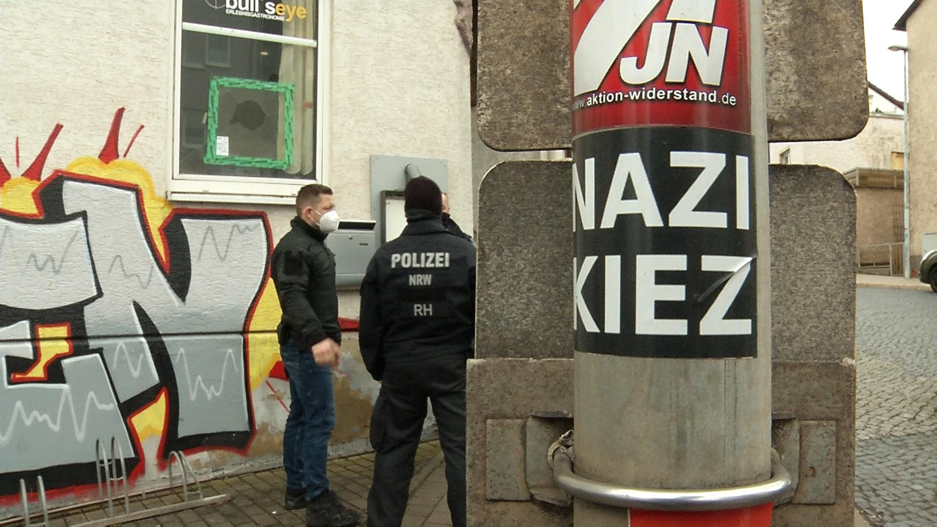 Polizisten stehen vor einer Gaststätte, an einem Pfahl ist ein Aufkleber mit der Aufschrift "Nazi Kiez" zu sehen.