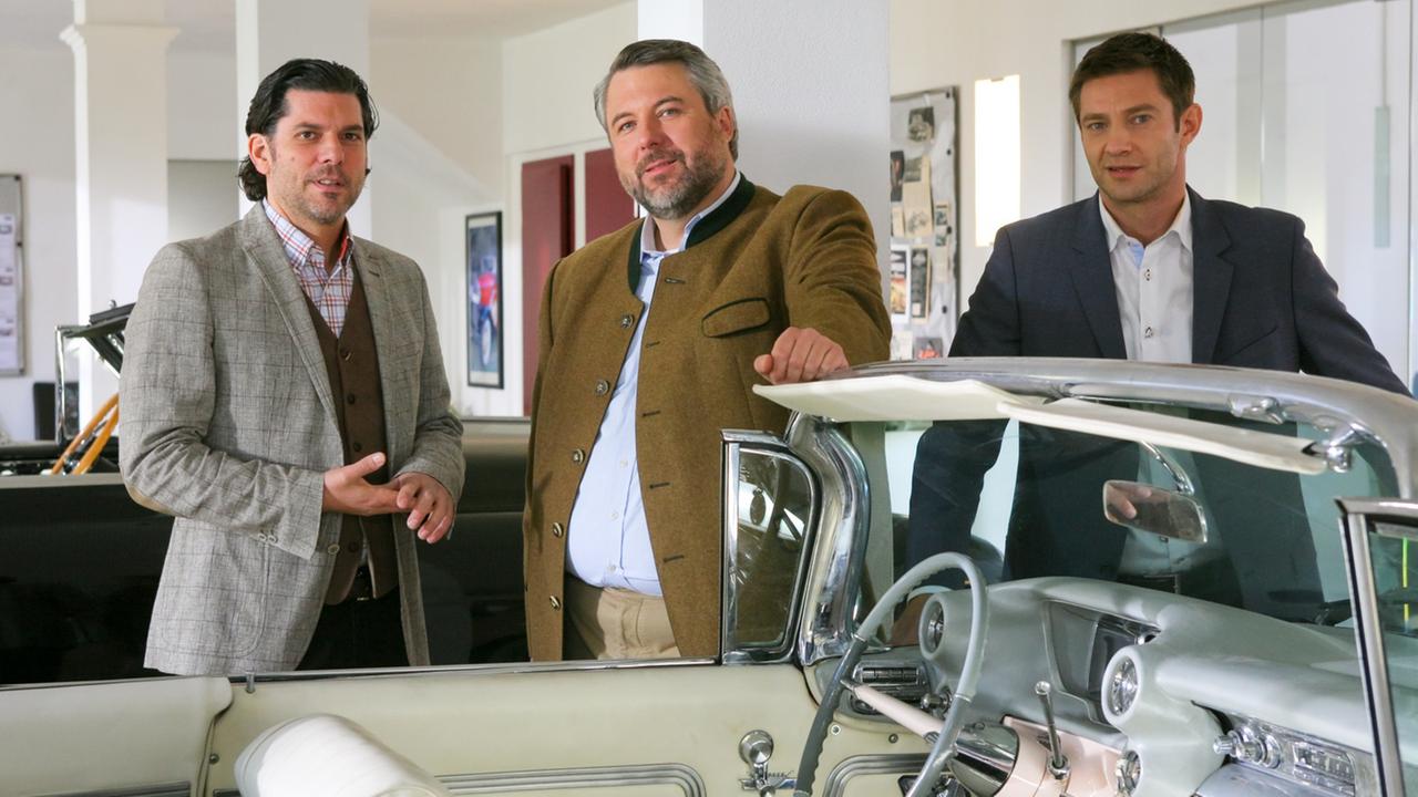 Die Ermittler Anton Stadler und Sven Hansen (Dieter Fischer, m.; Igor Jeftic, r.) zusammen mit Zachinger (Gregory Brian Waldis, l.) vor einem Oldtimer.