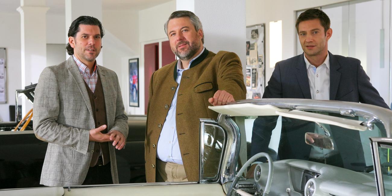 Die Ermittler Anton Stadler und Sven Hansen (Dieter Fischer, m.; Igor Jeftic, r.) zusammen mit Zachinger (Gregory Brian Waldis, l.) vor einem Oldtimer.