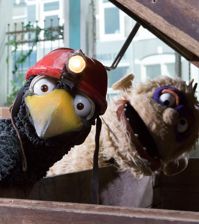 Monster und Rabe Rudi, mit Helm und Lampe auf dem Kopf, schauen erschrocken über die geöffnete Truhe hinweg.