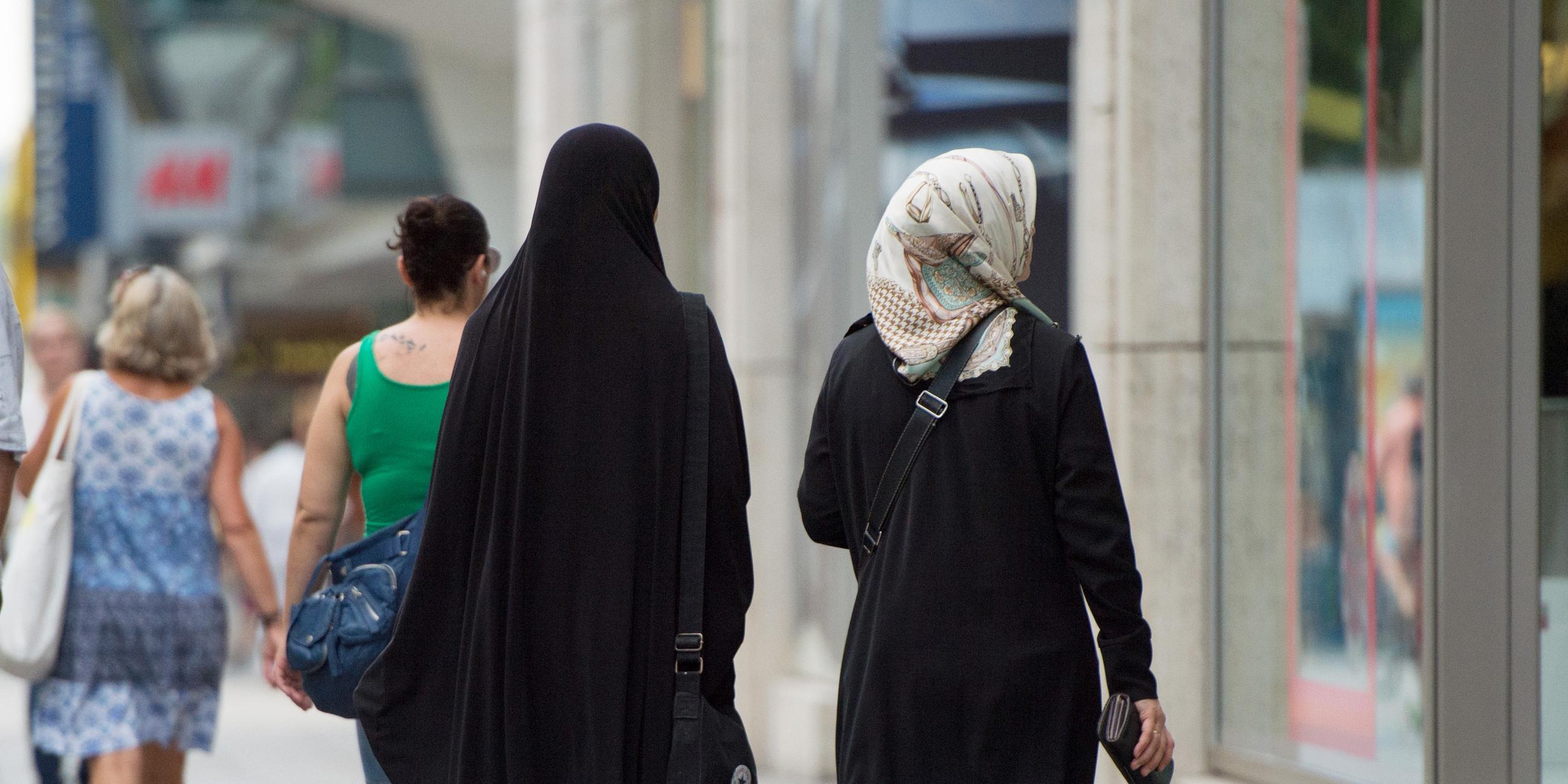 Zwei Frauen mit Kopftuch und langer Oberbekleidung gehen eine Straße entlang.