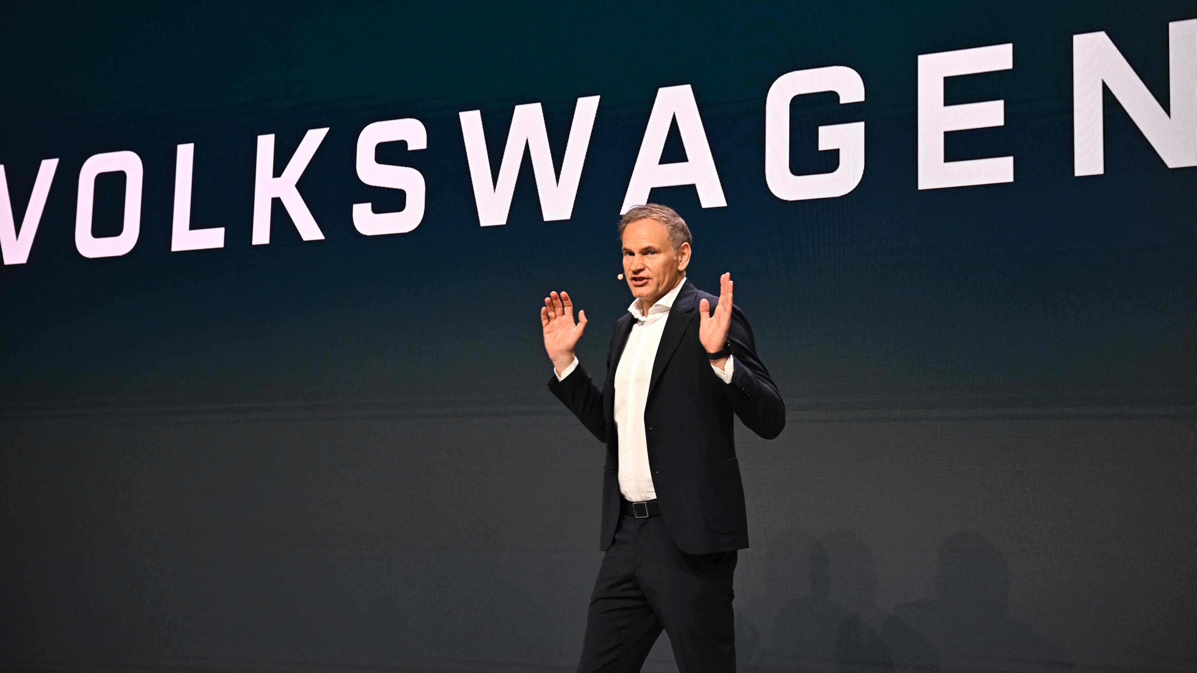 VW-Chef Oliver Blume vor auf Bühne, im Hintergrund groß zu lesen: "Volkswagen"