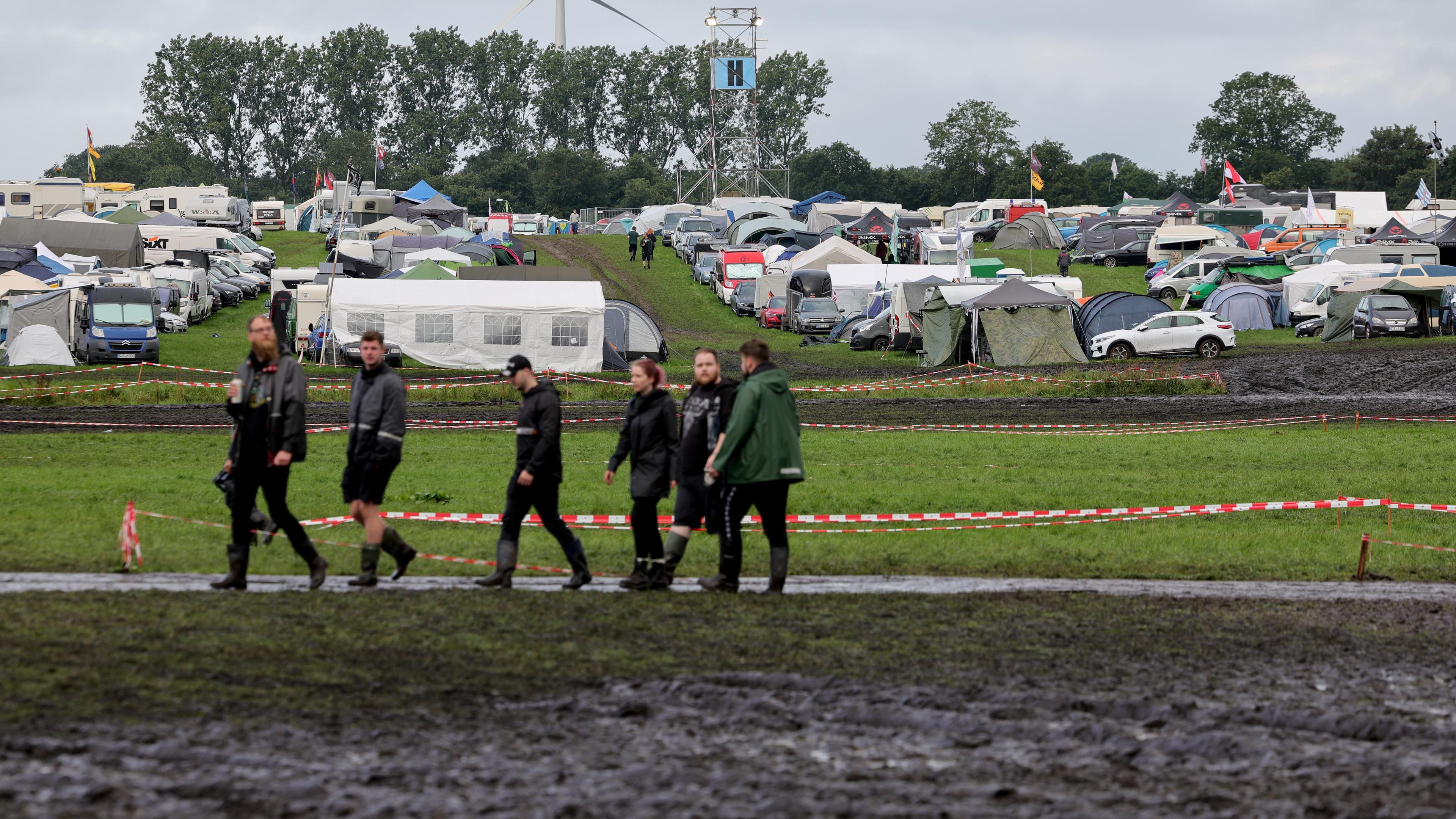 Schleswig-Holstein, Wacken: Metal-Fans sind am frühen Morgen auf dem vom Regen aufgeweichten und schlammigen Festivalgelände unterwegs.