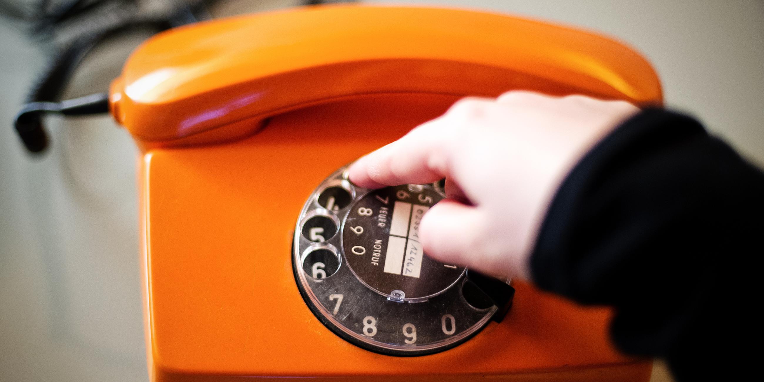 Eine Hand dreht an der Wählscheibe eines orangen Telefons.