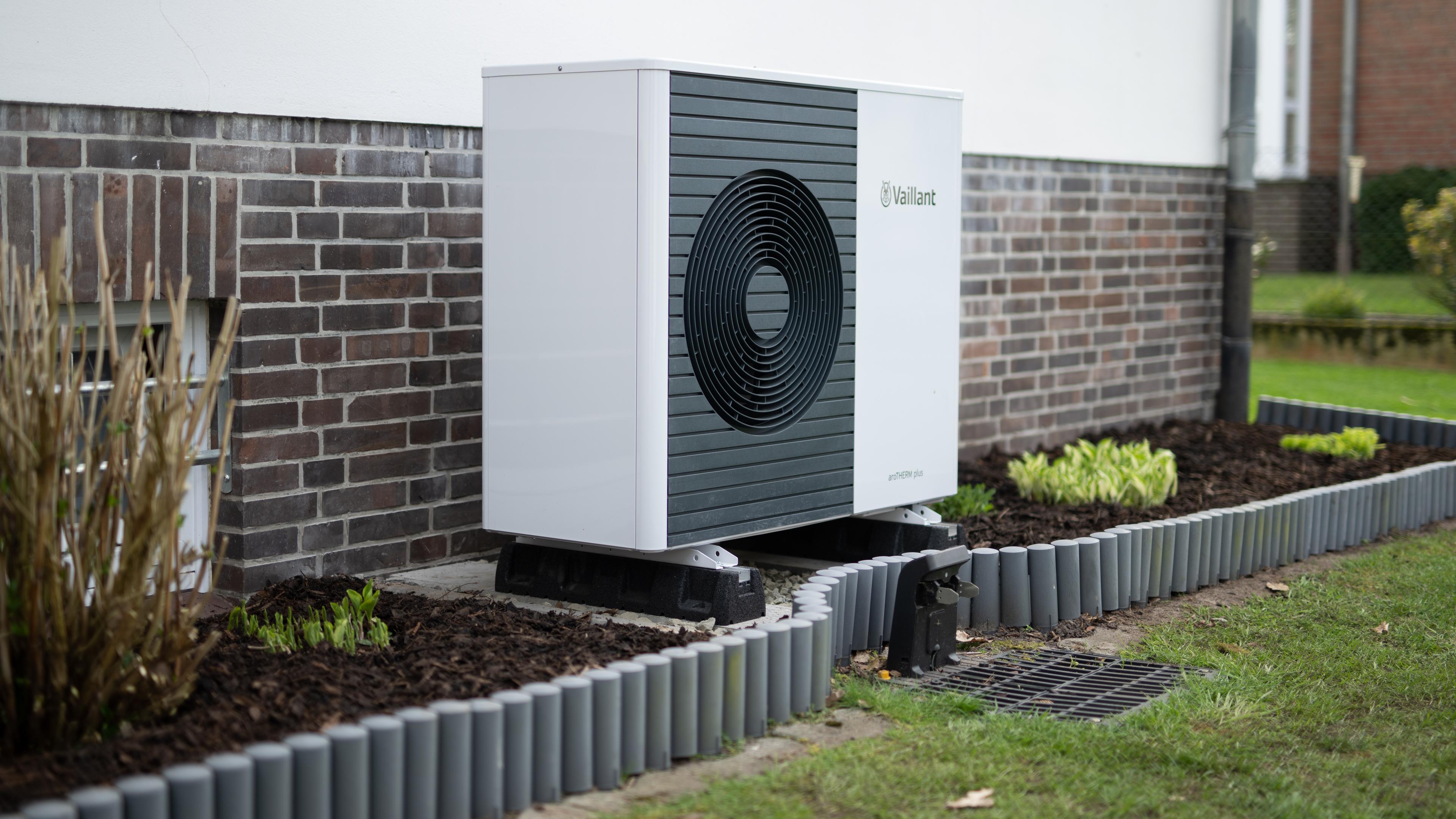 Die Lüftungsanlage einer Wärmepumpe steht vor der Fassade eines Einfamilienhauses im Garten.
