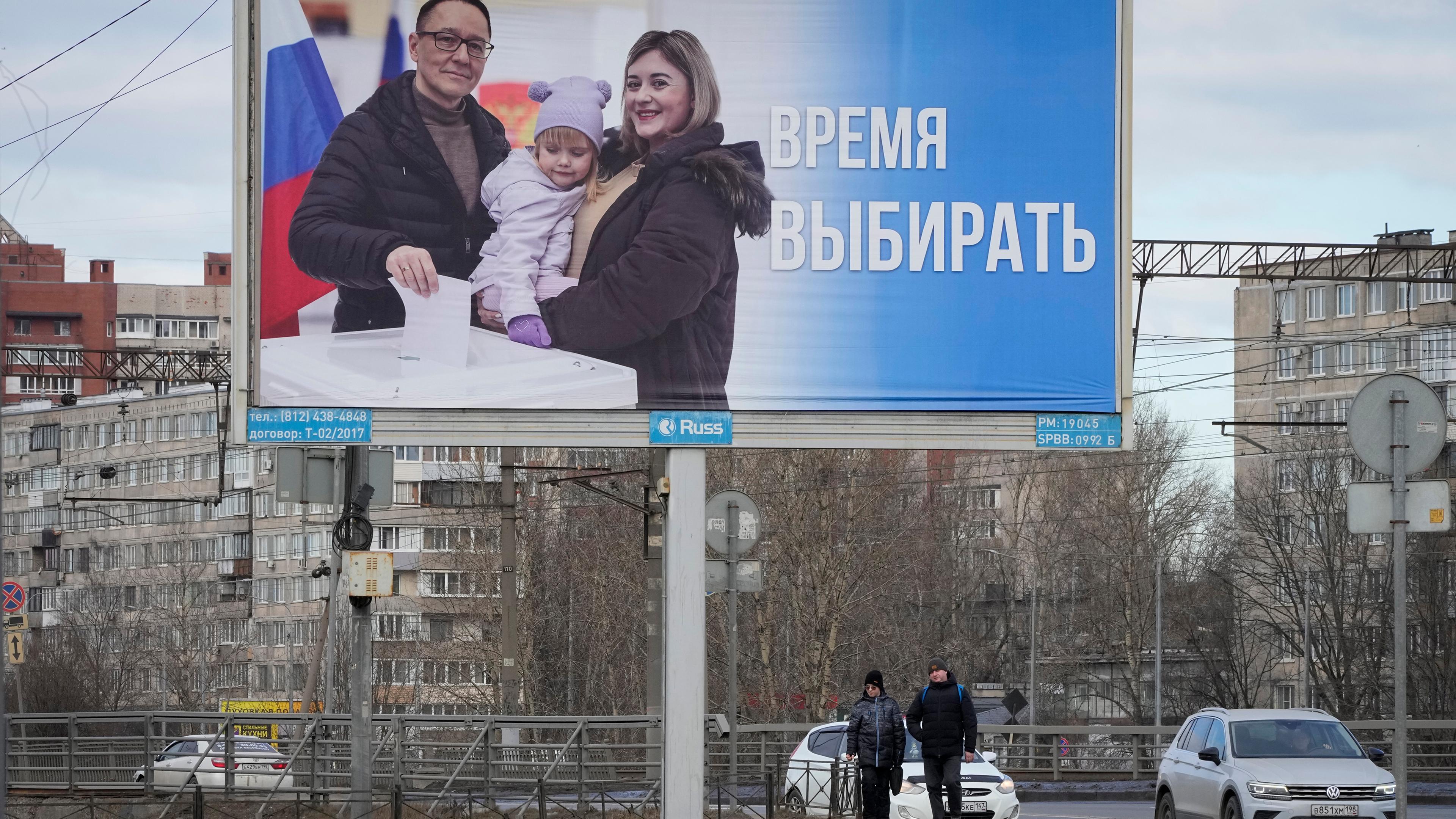 Russland, St. Petersburg: Menschen gehen an einem Plakat vorbei, das für die bevorstehenden Präsidentschaftswahlen wirbt und auf dem auf Russisch steht: "Zeit zu wählen".