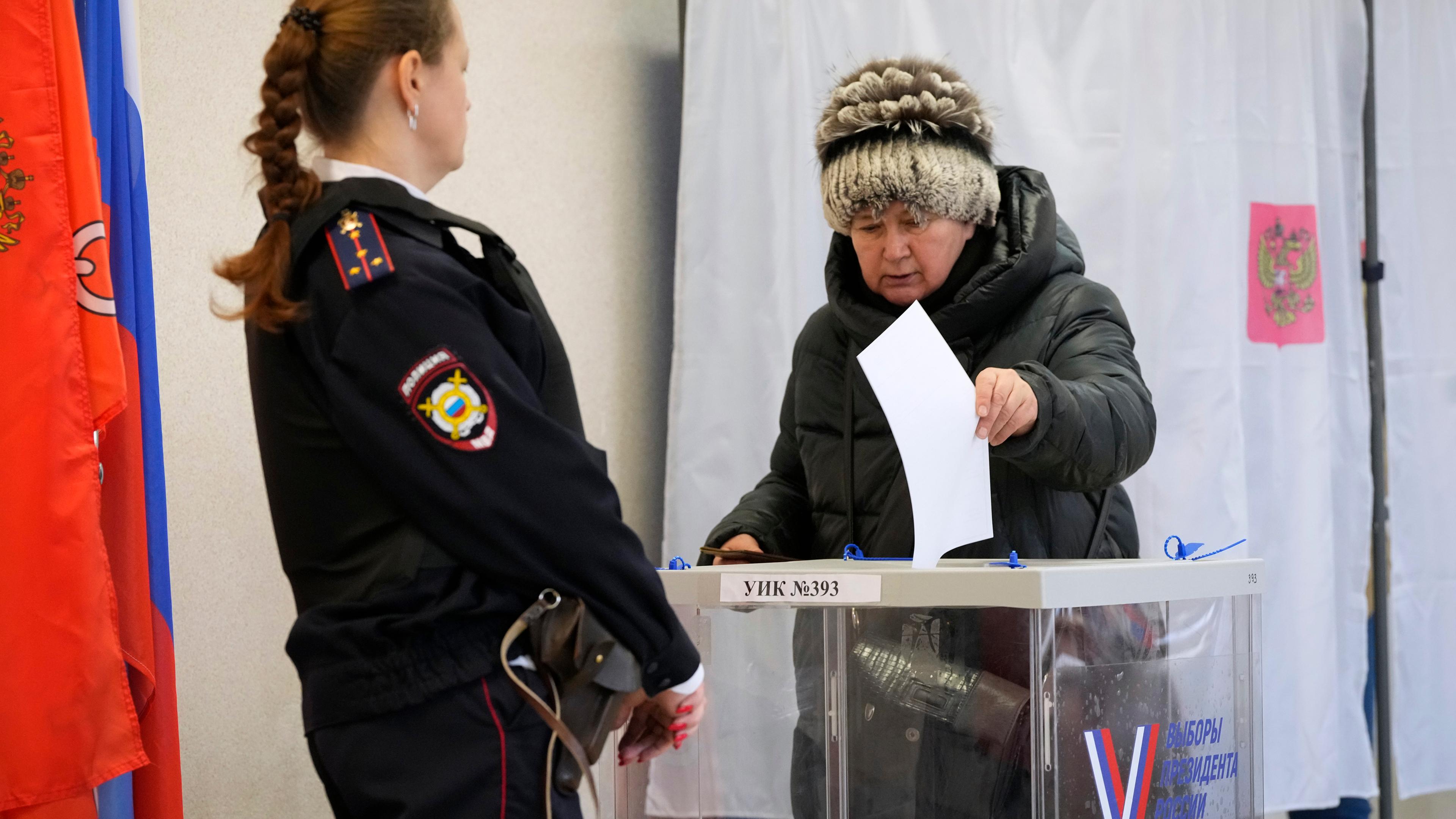 Eine Frau gibt ihre Stimme ab, während eine Polizistin ein Wahllokal während der Präsidentschaftswahl in St. Petersburg, bewacht. 