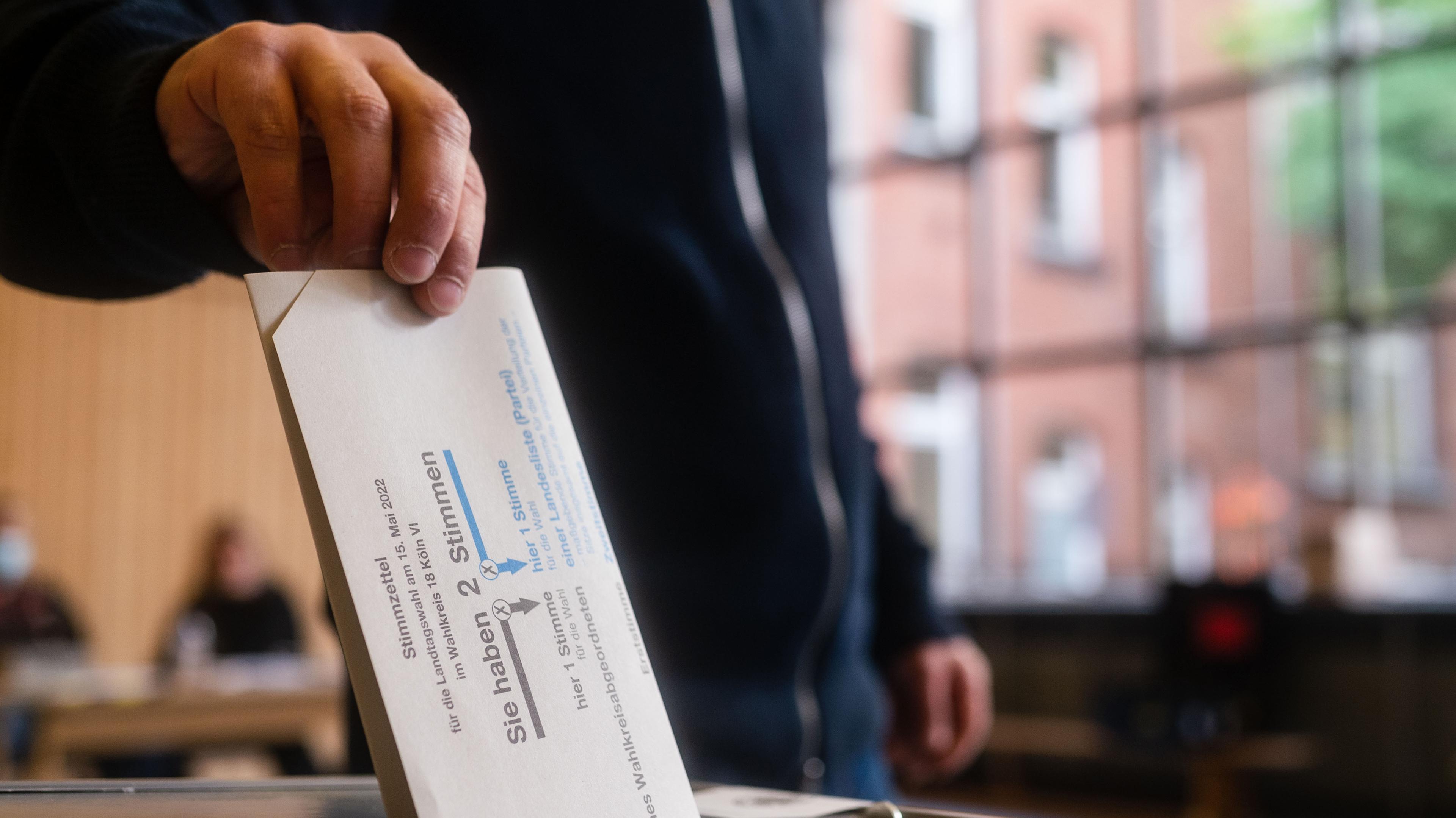 Ein Wähler/ eine Wählerin legt ihren Zetel in die Wahlurne.