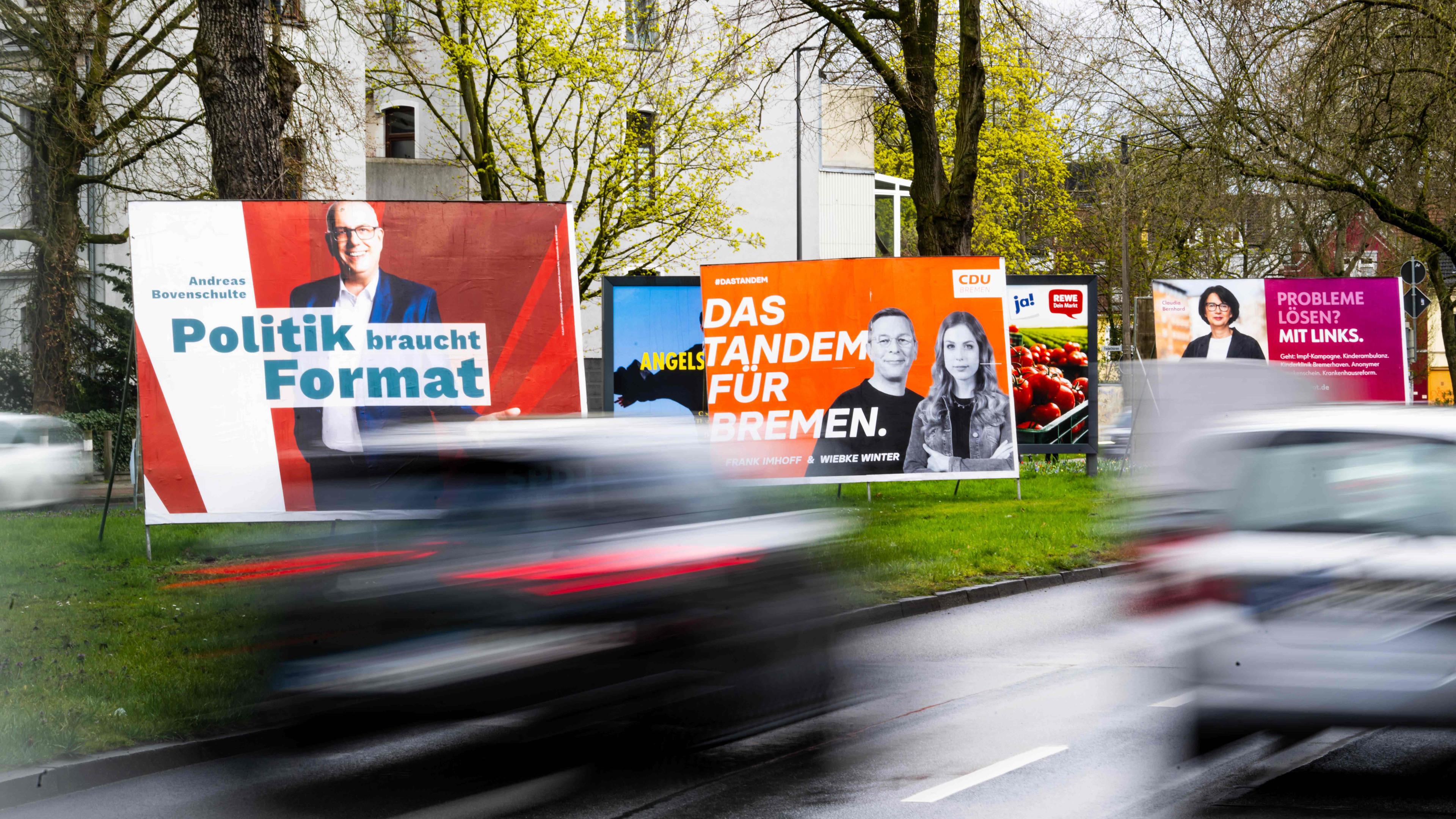 Wahlplakate verschiedener Parteien stehen am Straßenrand. 
