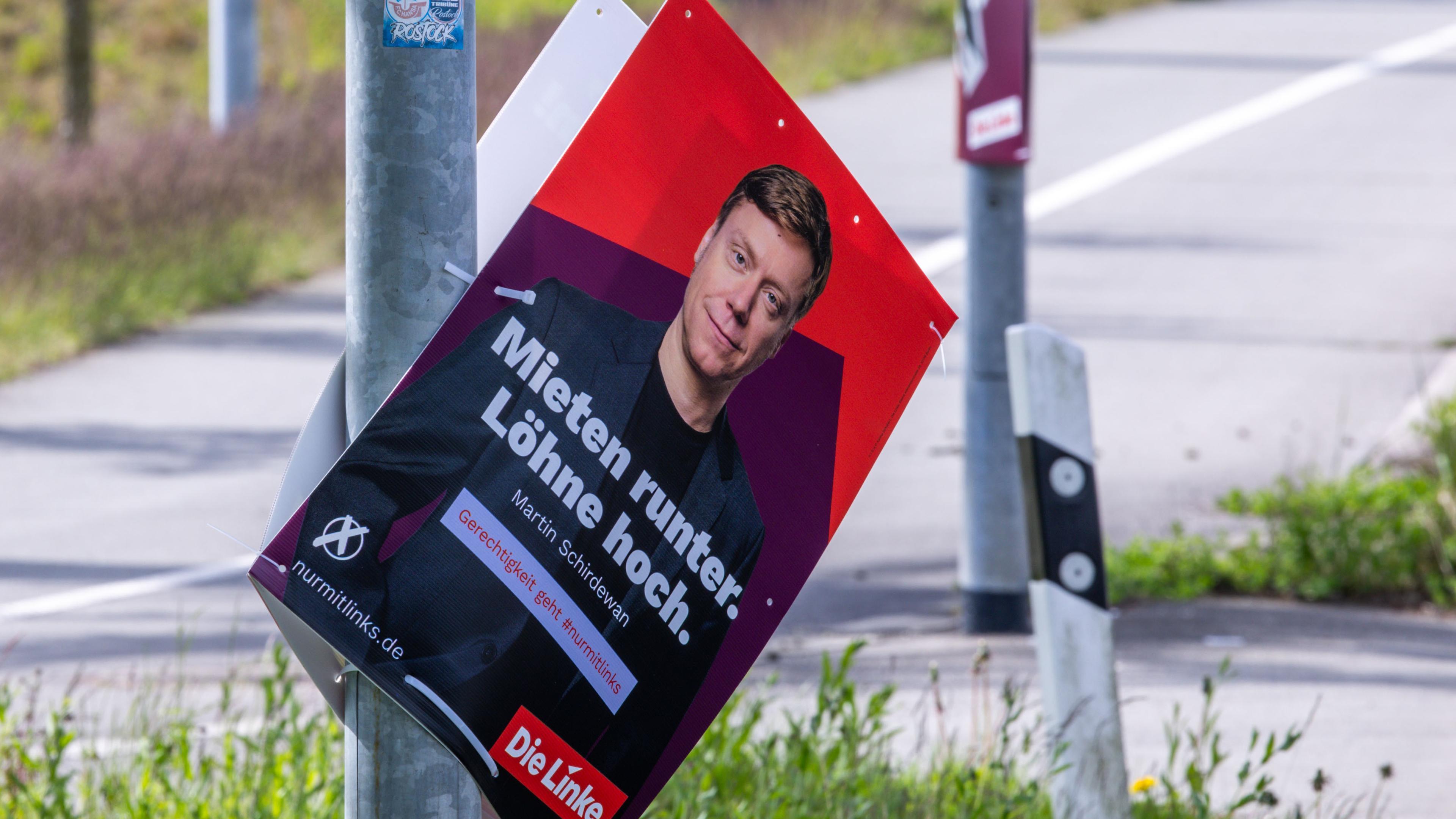 Ein Wahlplakat der Partei Die Linke hängt an einem Laternenmast einer Straße.