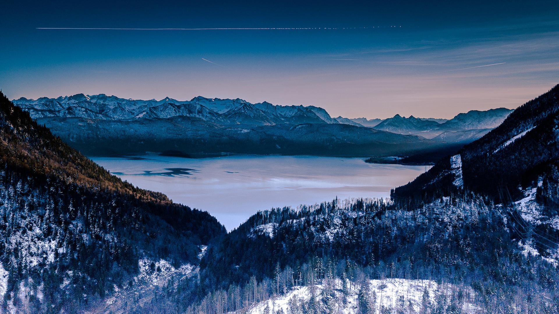Der Walchensee inmitten einer teilweise verschneiten Landschaft in der Dämmerung.
