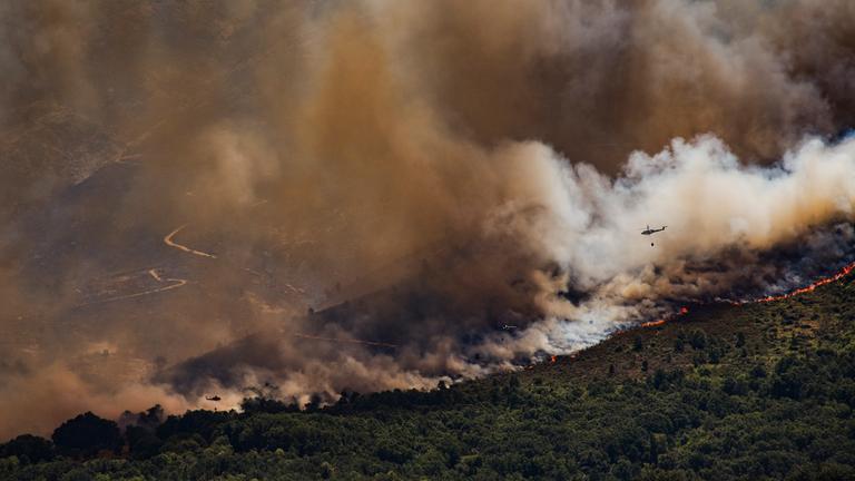 Ein Löschhubschrauber fliegt über einer dichten Rauchsäule während eines Waldbrandes.