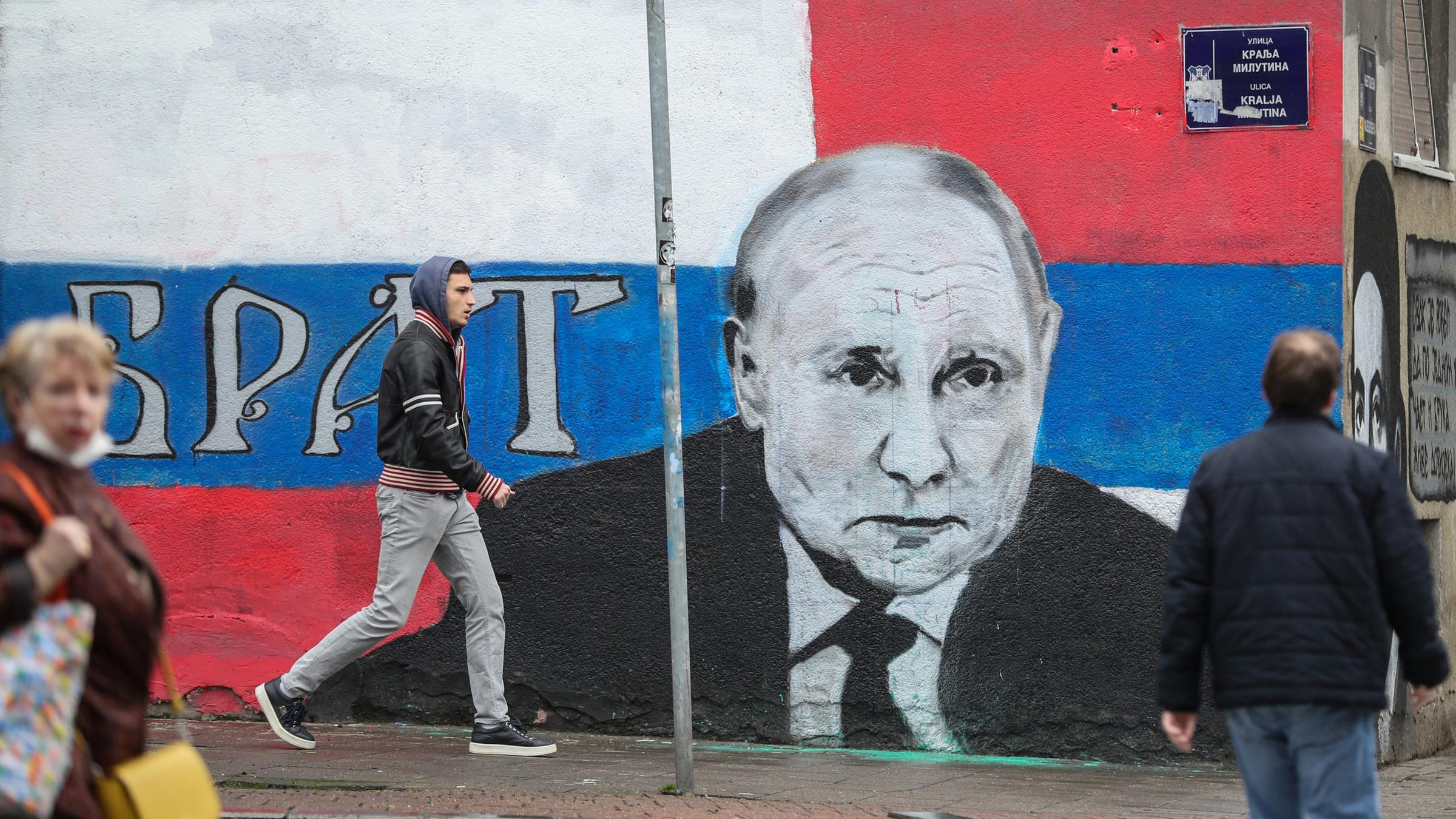 Menschen in Belgrad gehen neben einem Graffiti, das den russischen Präsidenten Wladimir Putin darstellt, vorbei.