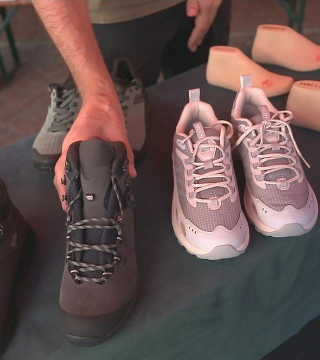 Verschiedene Wanderschuhe auf einem Tisch. Ein Mensch hebt einen hoch.