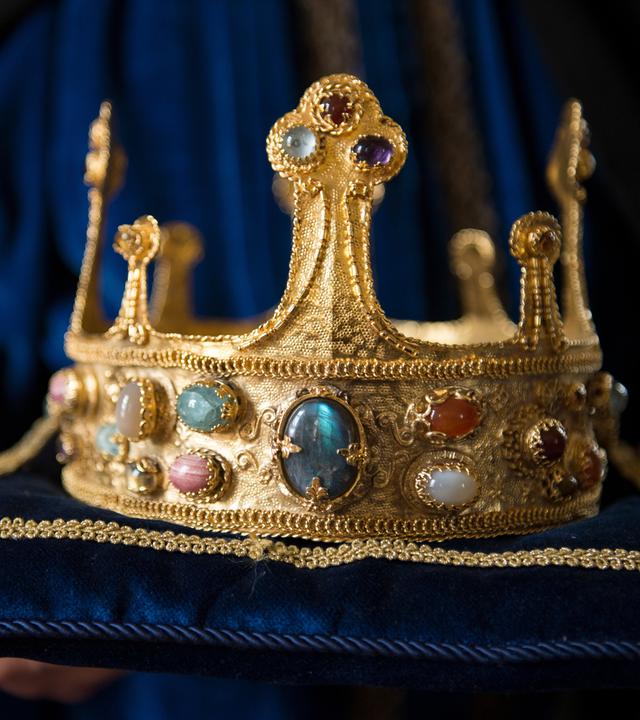 Eine goldene Krone liegt auf einem blauen Kissen.