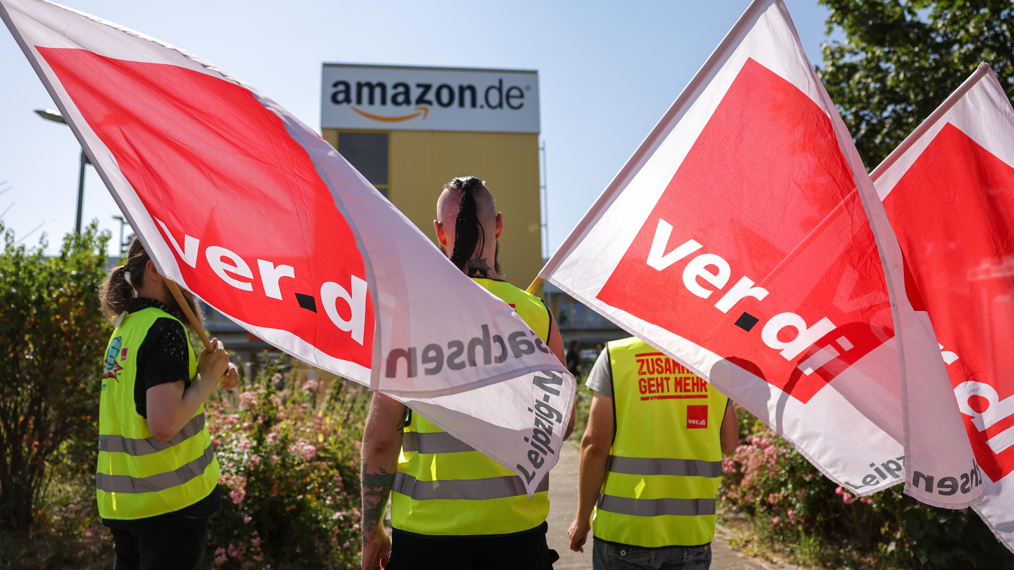 Streikende stehen mit Fahnen von Verdi vor einem Verteilzentrum des Online-Händlers Amazon.