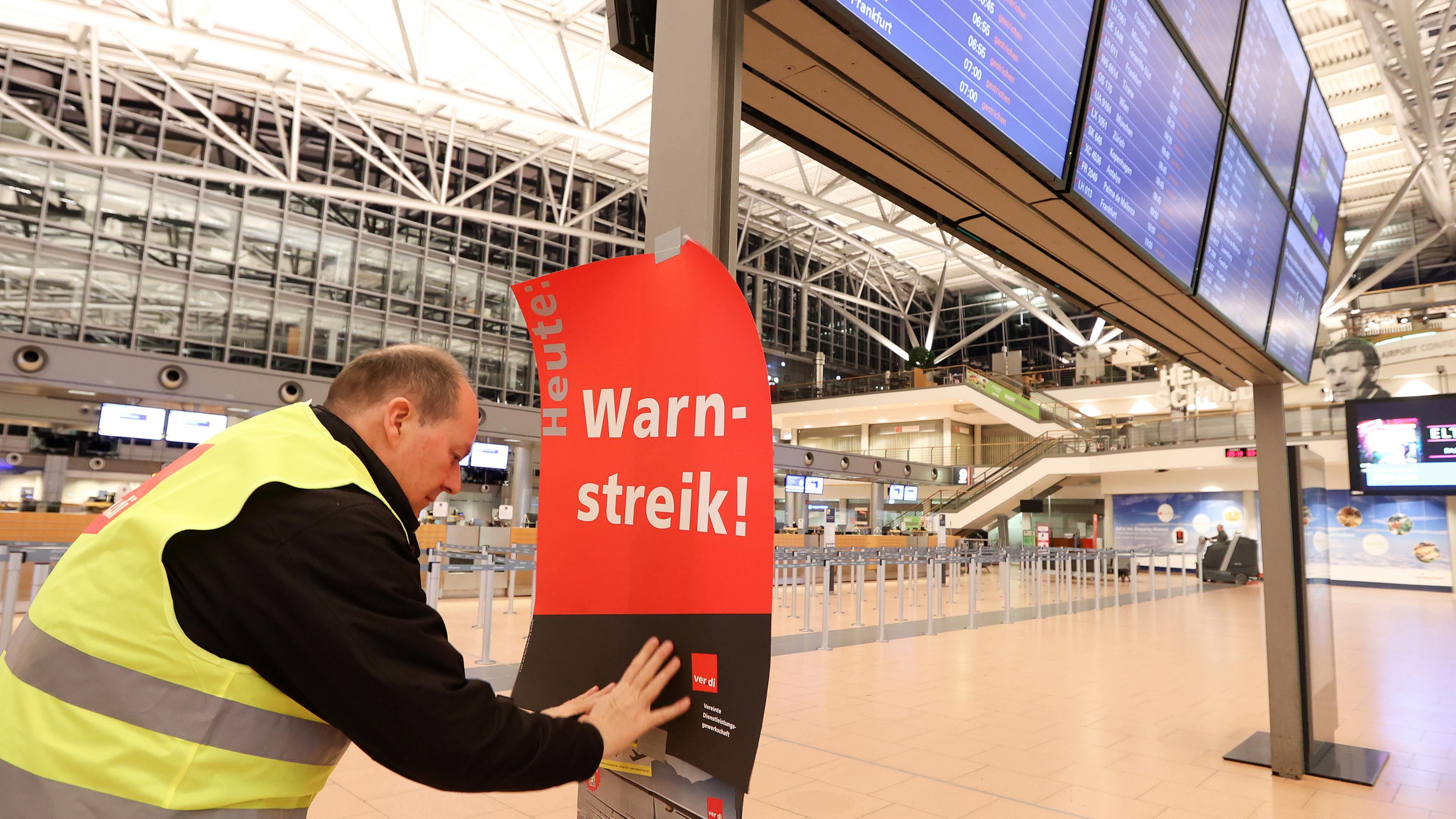 Ein Gewerkschaftsvertreter klebt ein Plakat mit der Aufschrift "Warnstreik!" an die Anzeigetafel im leeren Terminal 2 am Hamburger Flughafen. 