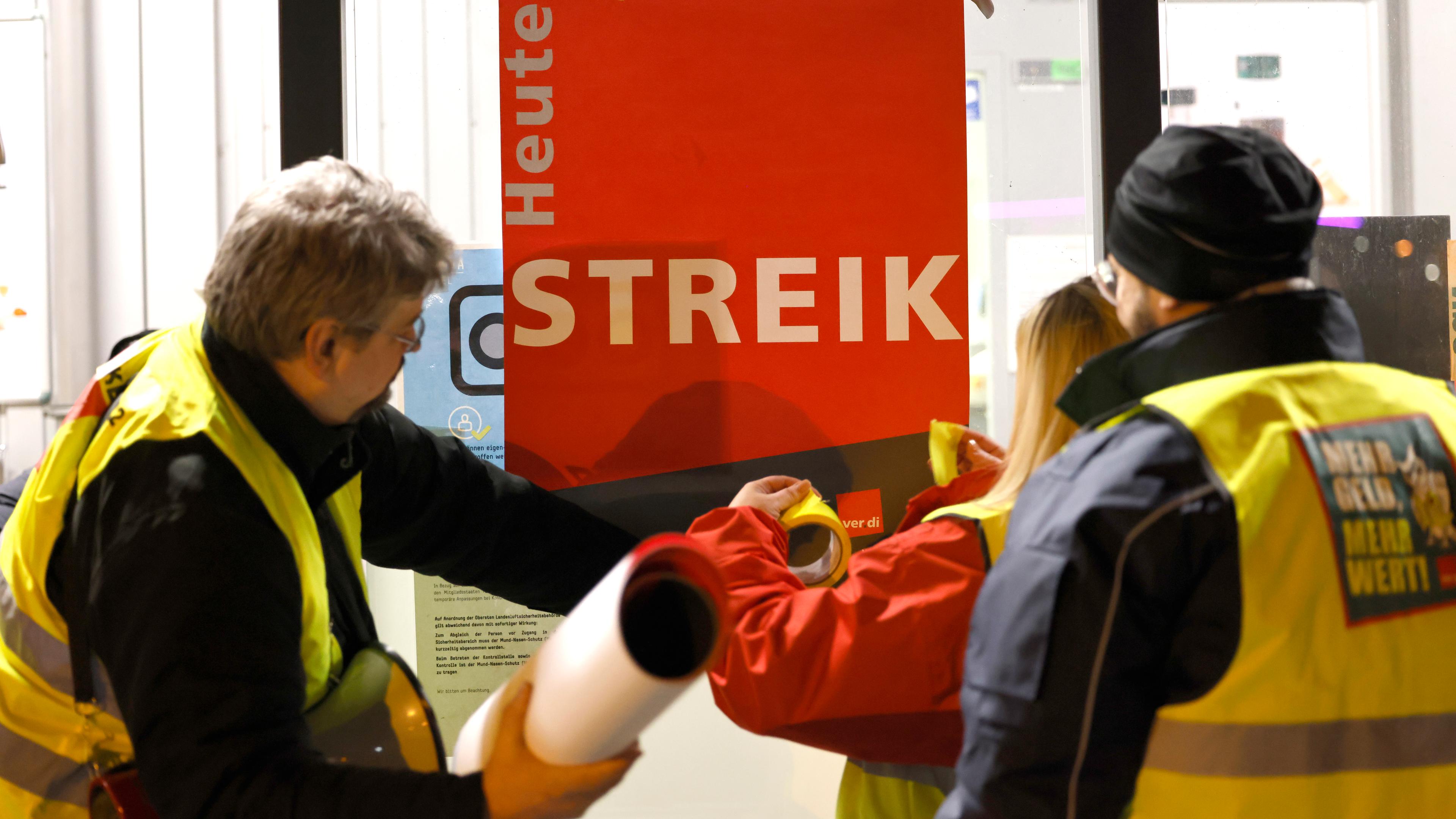 Streikende kleben ein Plakat mit der Aufschrift «Heute Streik» an eine Scheibe. Airport-Mitarbeiter der Luftsicherheit des Flughafens Köln Bonn streiken seit heute Abend für bessere Löhne