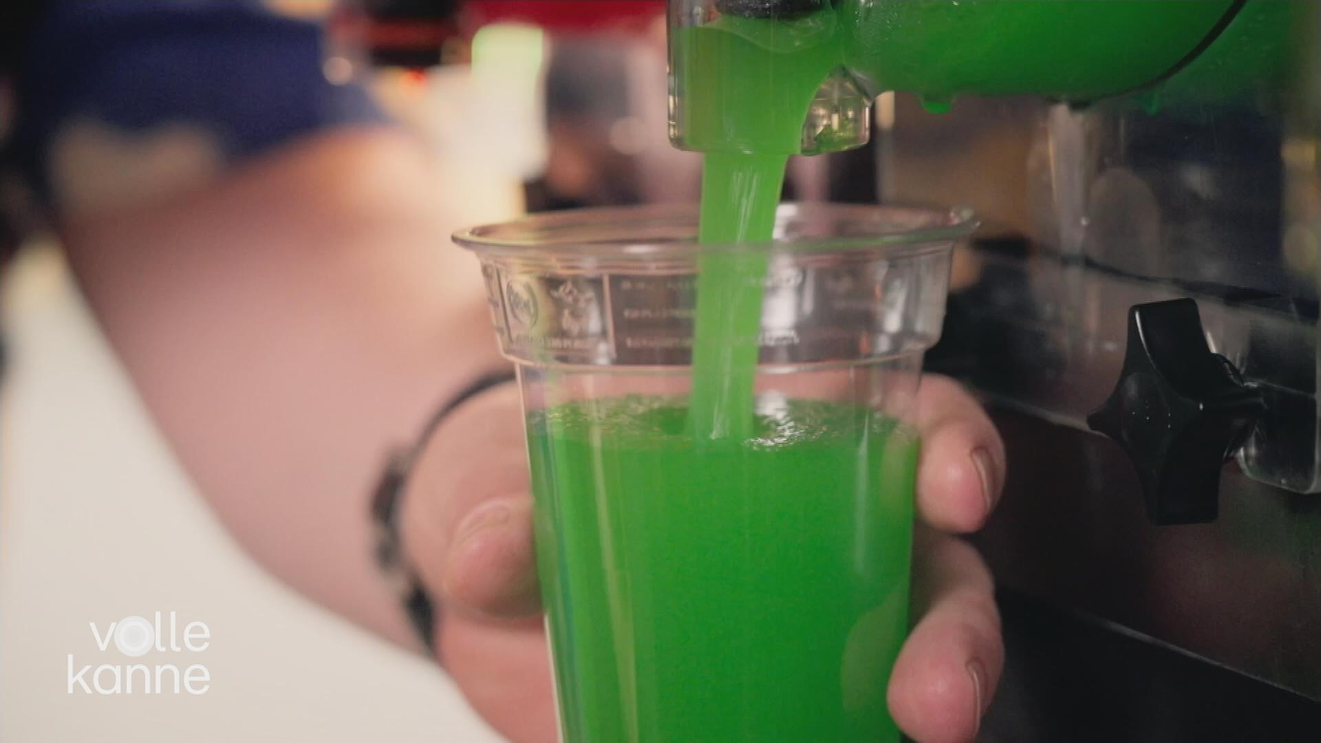 Eine Person füllt grünes Slush‑Eis in einen Becher.