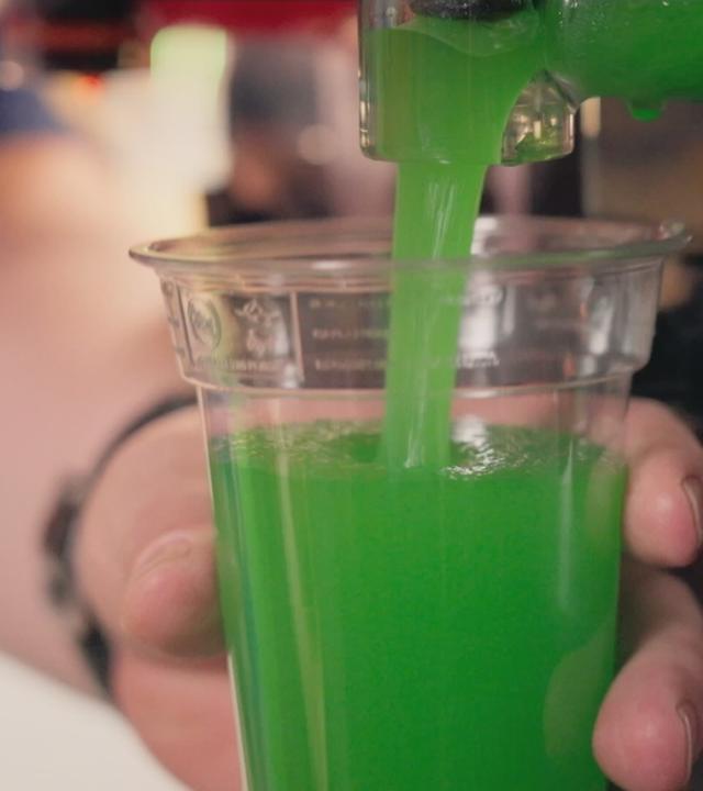 Eine Person füllt grünes Slush‑Eis in einen Becher.