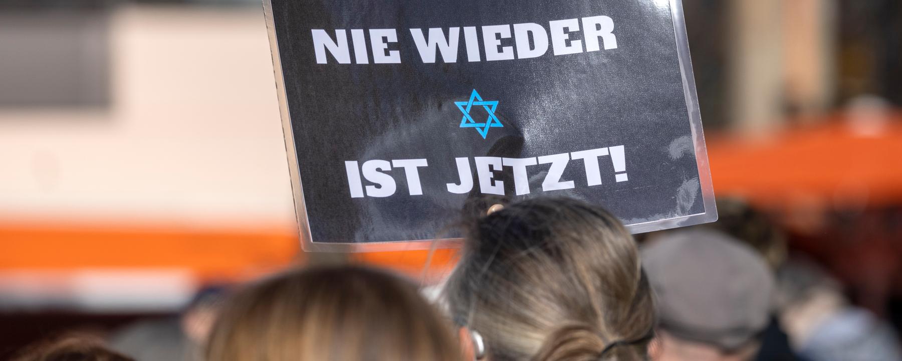 Ein Teilnehmer der Kundgebung «Aufstehen gegen Israelhass und Antisemitismus» hält ein Plakat mit der Aufschrift: ·Nie wieder ist jetzt· in die Höhe.