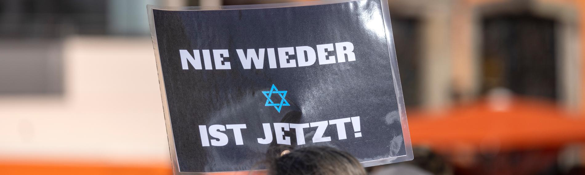 Ein Teilnehmer der Kundgebung «Aufstehen gegen Israelhass und Antisemitismus» hält ein Plakat mit der Aufschrift: ·Nie wieder ist jetzt· in die Höhe.