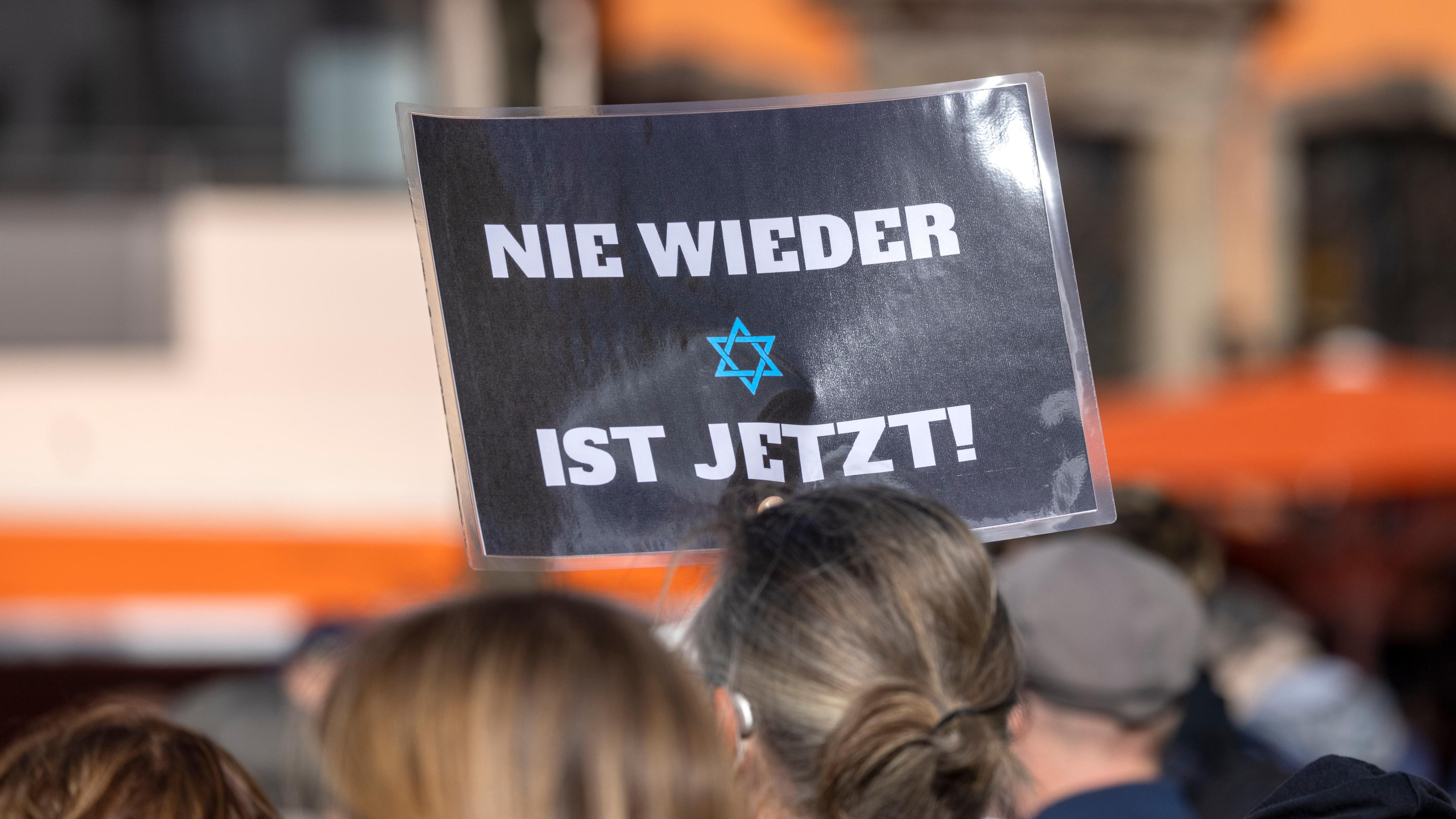 Ein Teilnehmer der Kundgebung «Aufstehen gegen Israelhass und Antisemitismus» hält ein Plakat mit der Aufschrift: ·Nie wieder ist jetzt· in die Höhe.