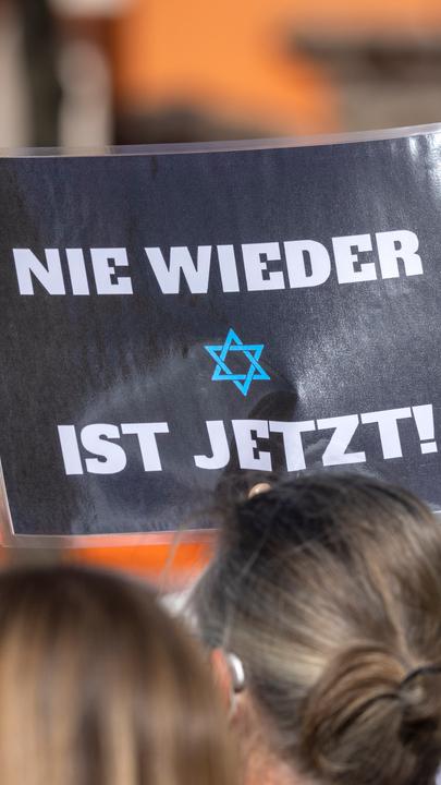 Ein Teilnehmer der Kundgebung «Aufstehen gegen Israelhass und Antisemitismus» hält ein Plakat mit der Aufschrift: ·Nie wieder ist jetzt· in die Höhe.