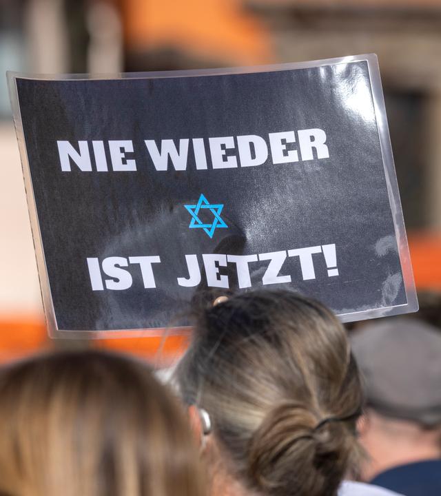 Ein Teilnehmer der Kundgebung «Aufstehen gegen Israelhass und Antisemitismus» hält ein Plakat mit der Aufschrift: ·Nie wieder ist jetzt· in die Höhe.