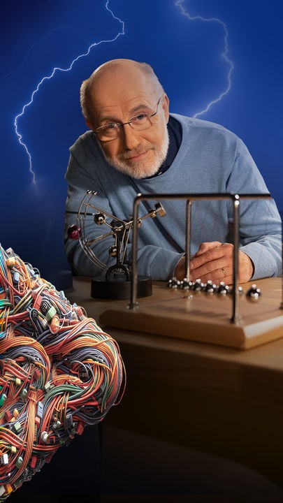 Harald Lesch steht neben einem Perpetuum-Mobile. Rechts im Bild deuten bunte Kabel ein X an und Biltze im Hinterrgund symbolisieren das Thema Energie