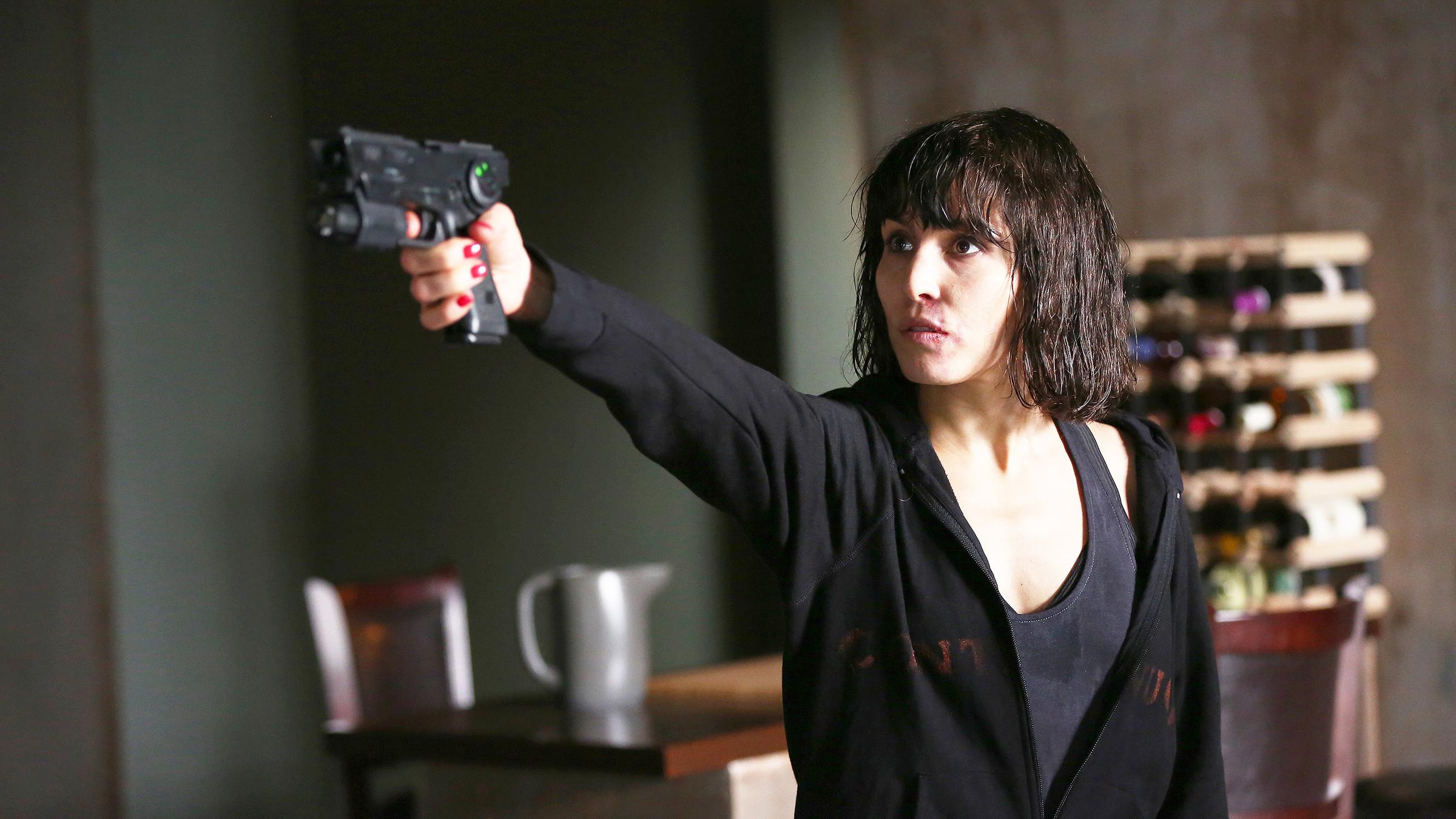 Wednesday (Noomi Rapace) steht mit gezogener Waffe in der Küche.