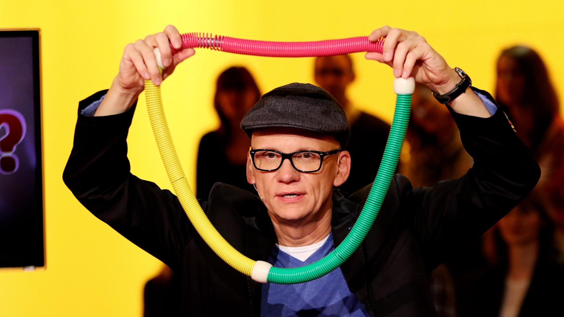 Ein Mann hält sich eine bunte, breite Kette vor den Kopf.
