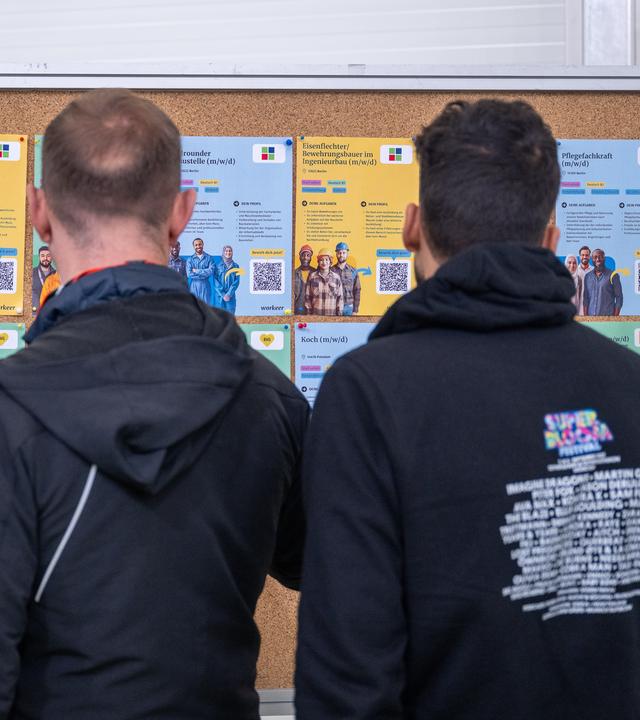 Drei geflüchtete Männer schauen sich eine Tafel mit Job-Möglichkeiten für Geflüchtete an.