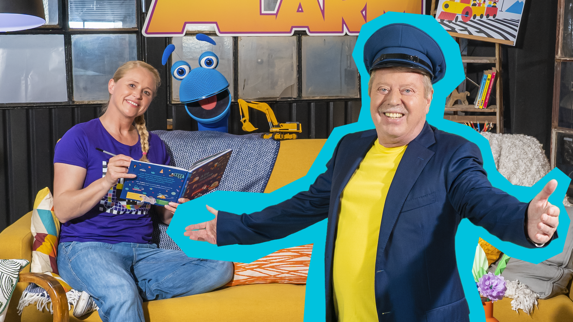 Singa sitzt lächelnd mit einem Buch in der Hand auf dem Sofa. Das SingDing schaut lachend hinter dem Sofa hervor. Volker Rosin steht mit ausgebreiteten Armen und einer Lokführermütze vor dem Sofa und lächelt ebenfalls in die Kamera.
