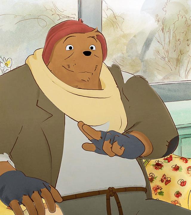 Bolero sitzt mitten im Wohnzimmer von Madame Tulipe in einem Sessel mit Blumenmuster. Er trägt einen Mantel, seine rote Mütze auf dem Kopf und einen cremefarbenen Schal um den Hals. Madame Tulipe schaut er lächelnd an.