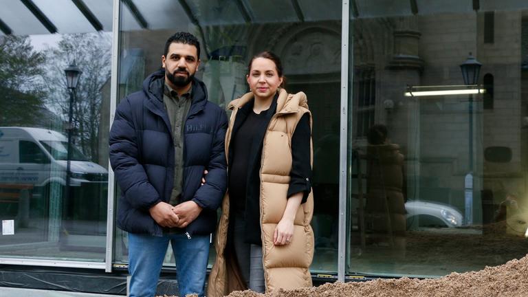 Nora und Soufyan Nechad stehen vor ihrem zukünftigen Optikergeschäft und schauen in die Kamera.