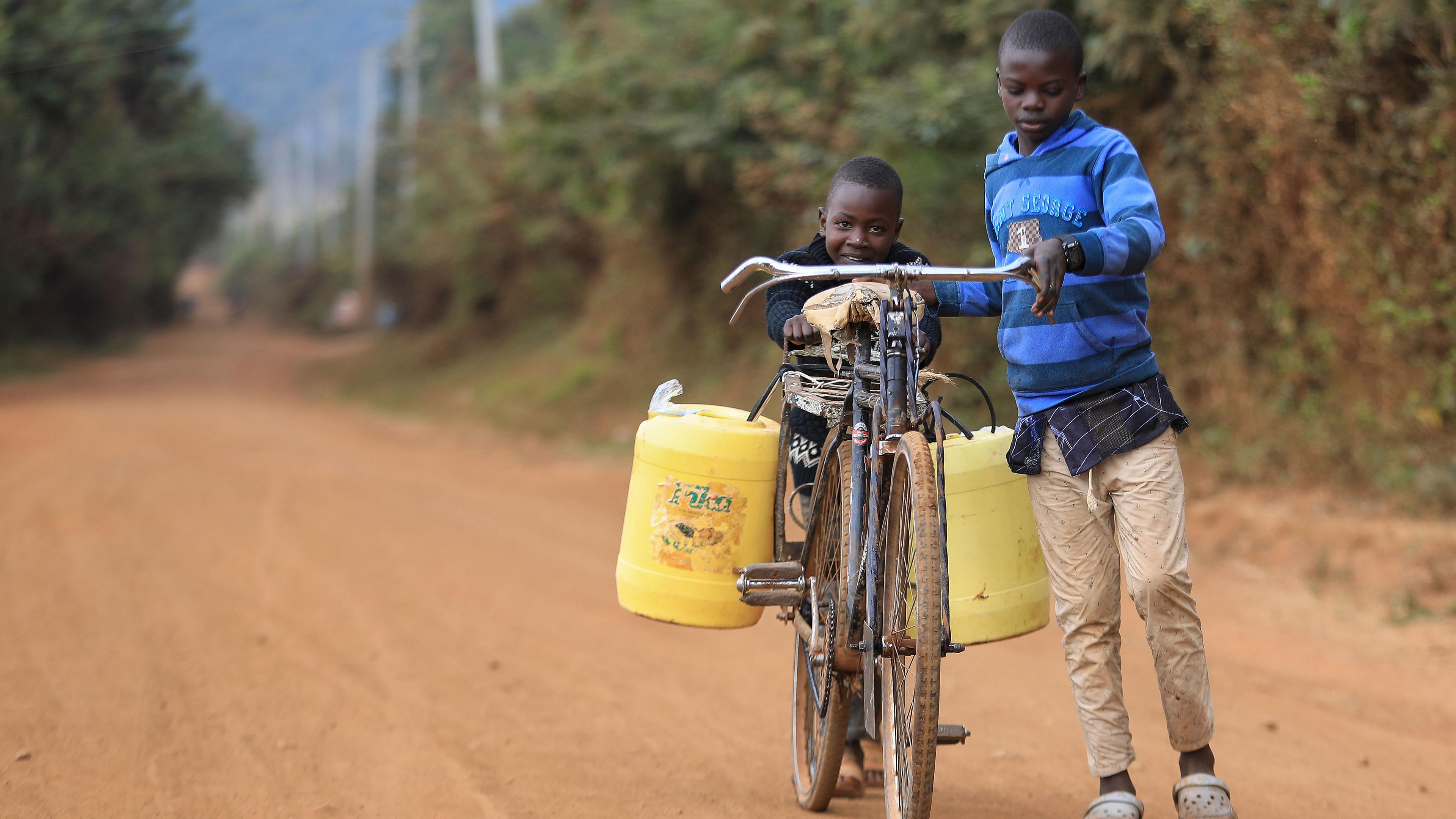Zwei kenianische jungs benutzen ein Fahrrad, um Wasser in Kanistern in der ländlichen Stadt Oldonyo Sabuk in Machakos (Kenia) zu holen, aufgenommen am 28.07.2020