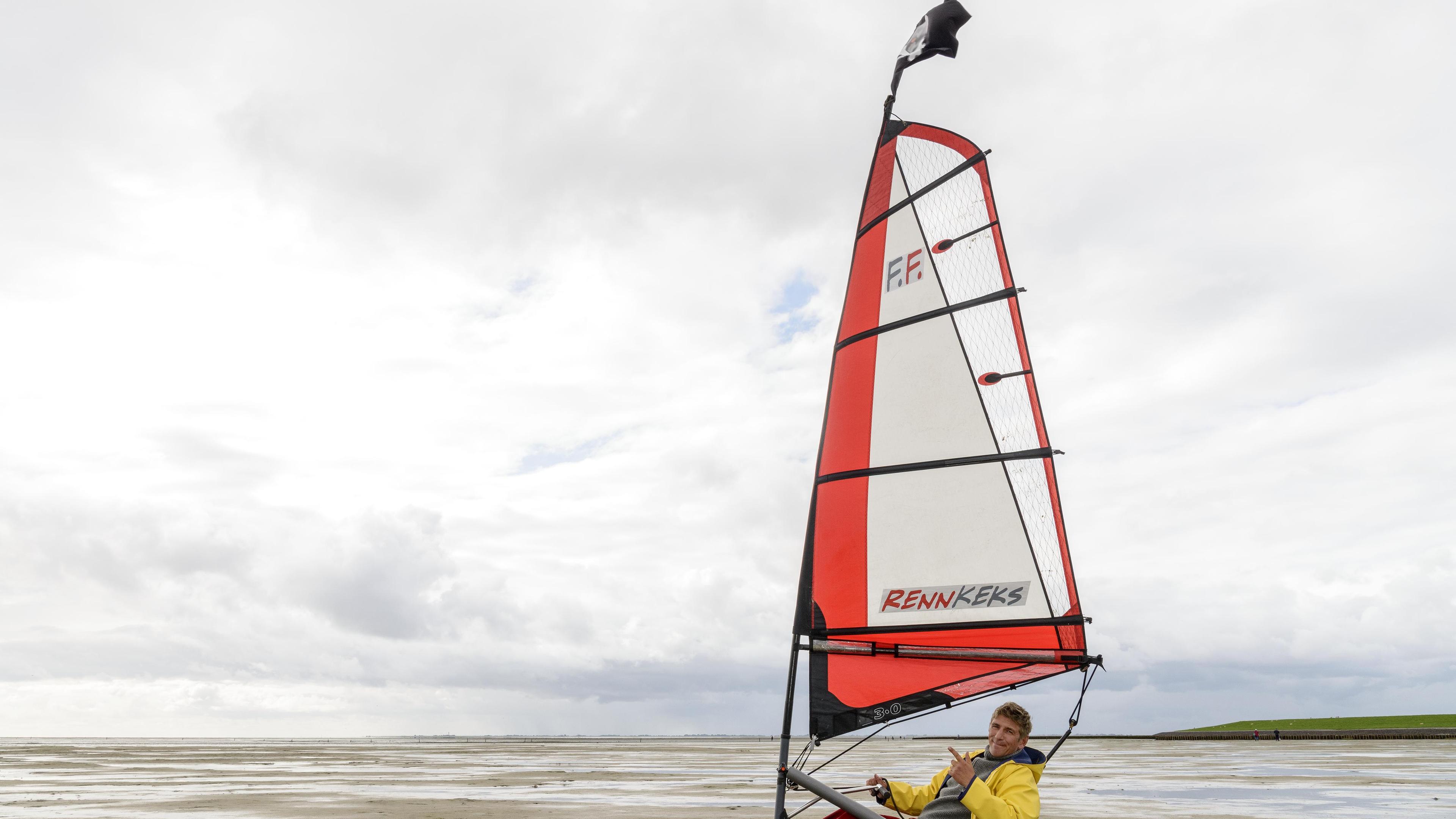 Fritz Fuchs sitzt in einem Strandsegler. Es ist Ebbe, das Meer hat sich zurückgezogen.