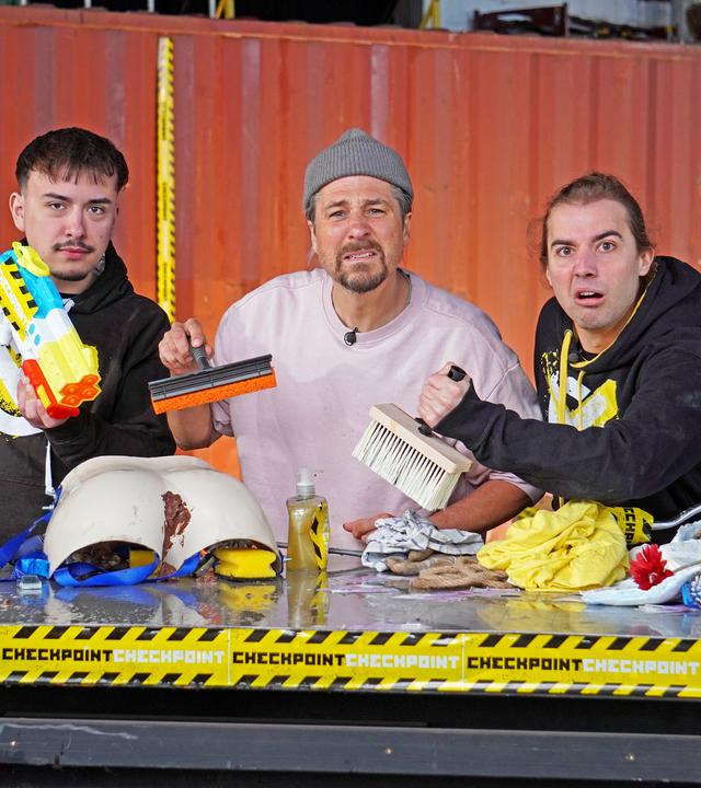 Moritz, Tommy Scheel und Leopold halten eine Wasserpistole, einen Fensterreiniger und eine Kleisterbürste in der Hand. Vor ihnen liegen diverse Utensilien auf dem Tisch.