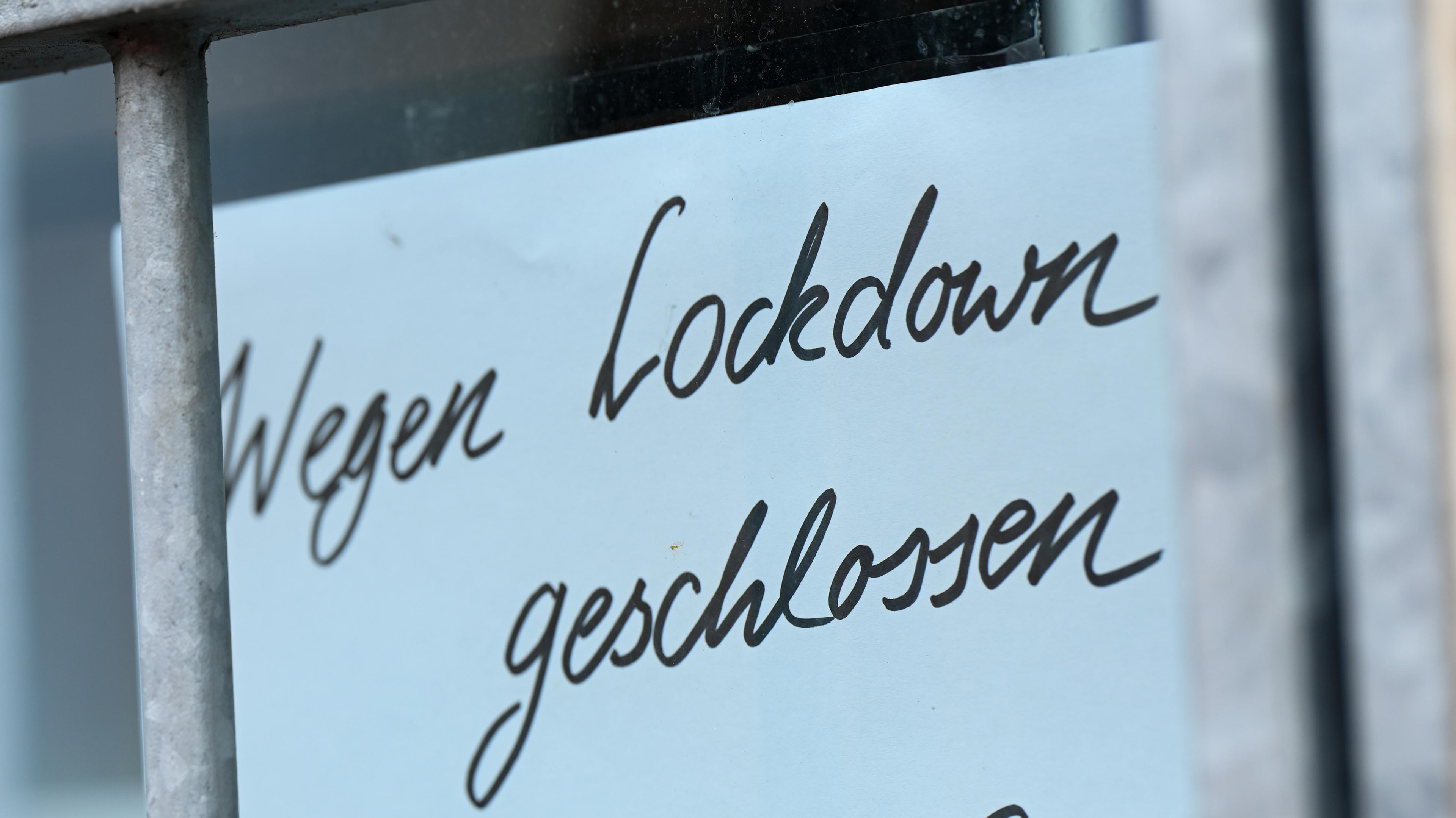 Auf dem Bild sieht man ein Schild, auf welchem "Wegen Lockdown geschlossen" steht. Es hängt in einem Fenster hinter Gitterstäben.