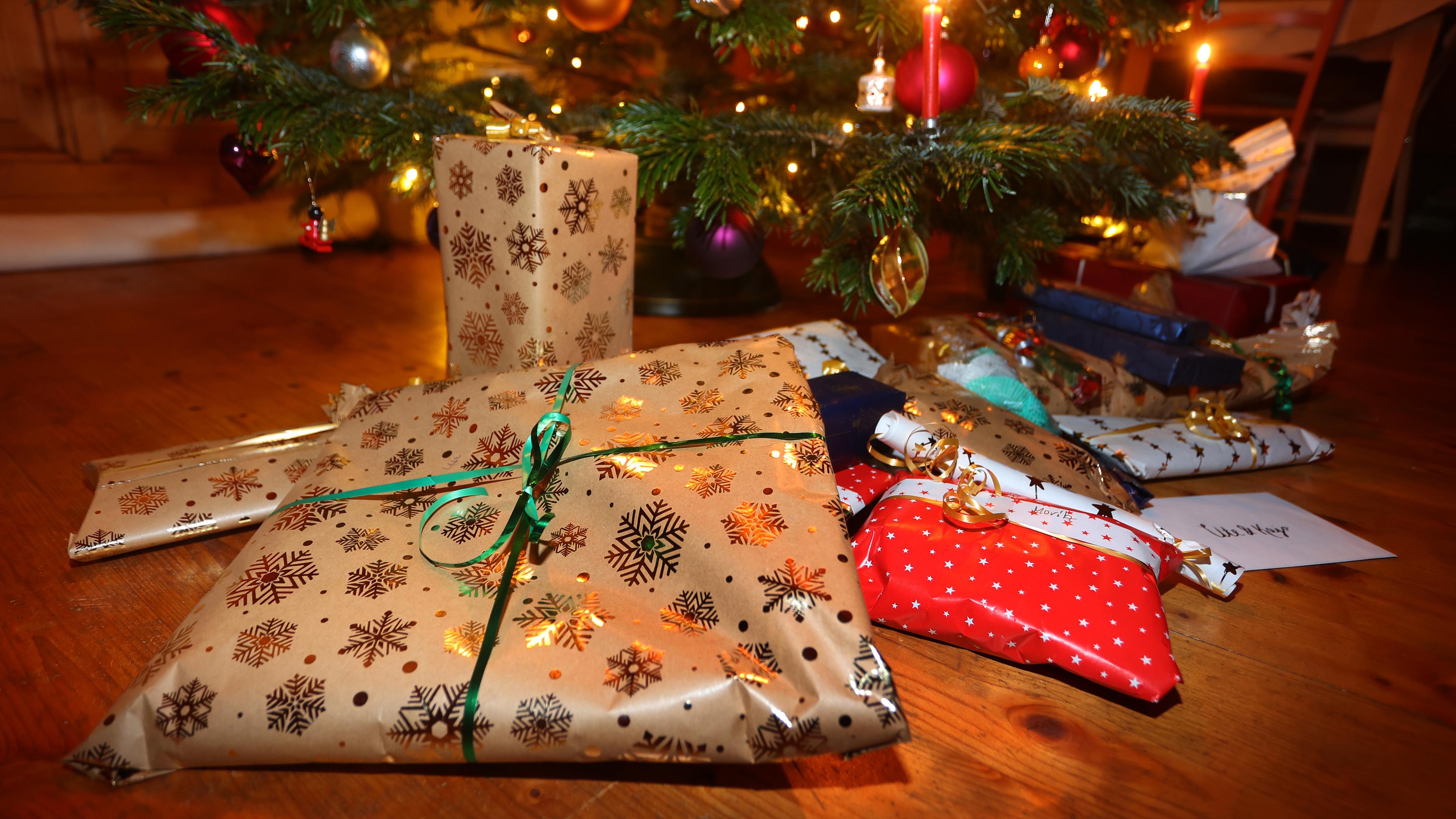Verpackte Geschenke liegen in einem Wohnzimmer unter einem festlich geschmücktem Weihnachtsbaum