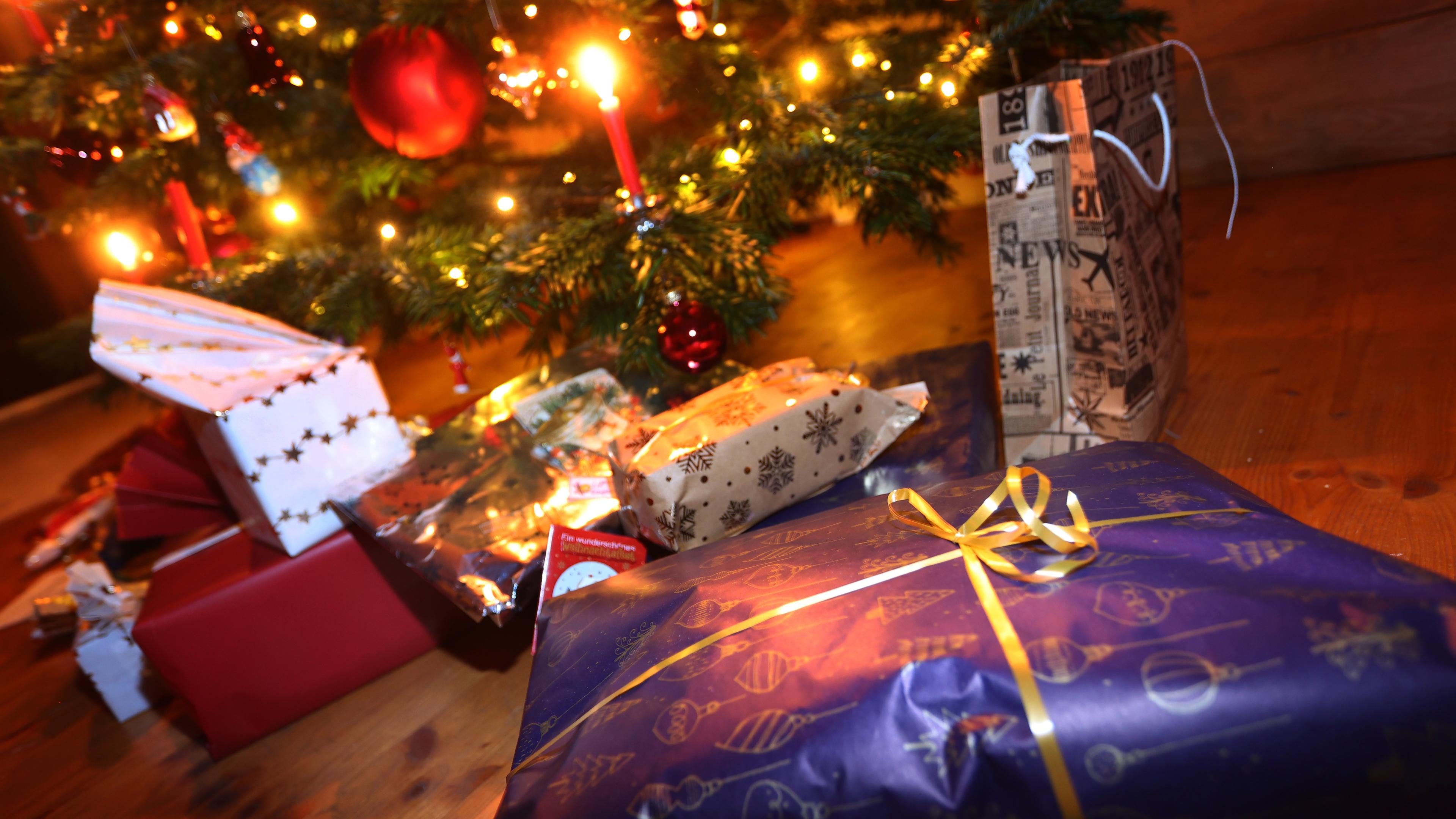 Verpackte Geschenke liegen in einem Wohnzimmer unter einem festlich geschmücktem Weihnachtsbaum, aufgenommen am 24.12.2021